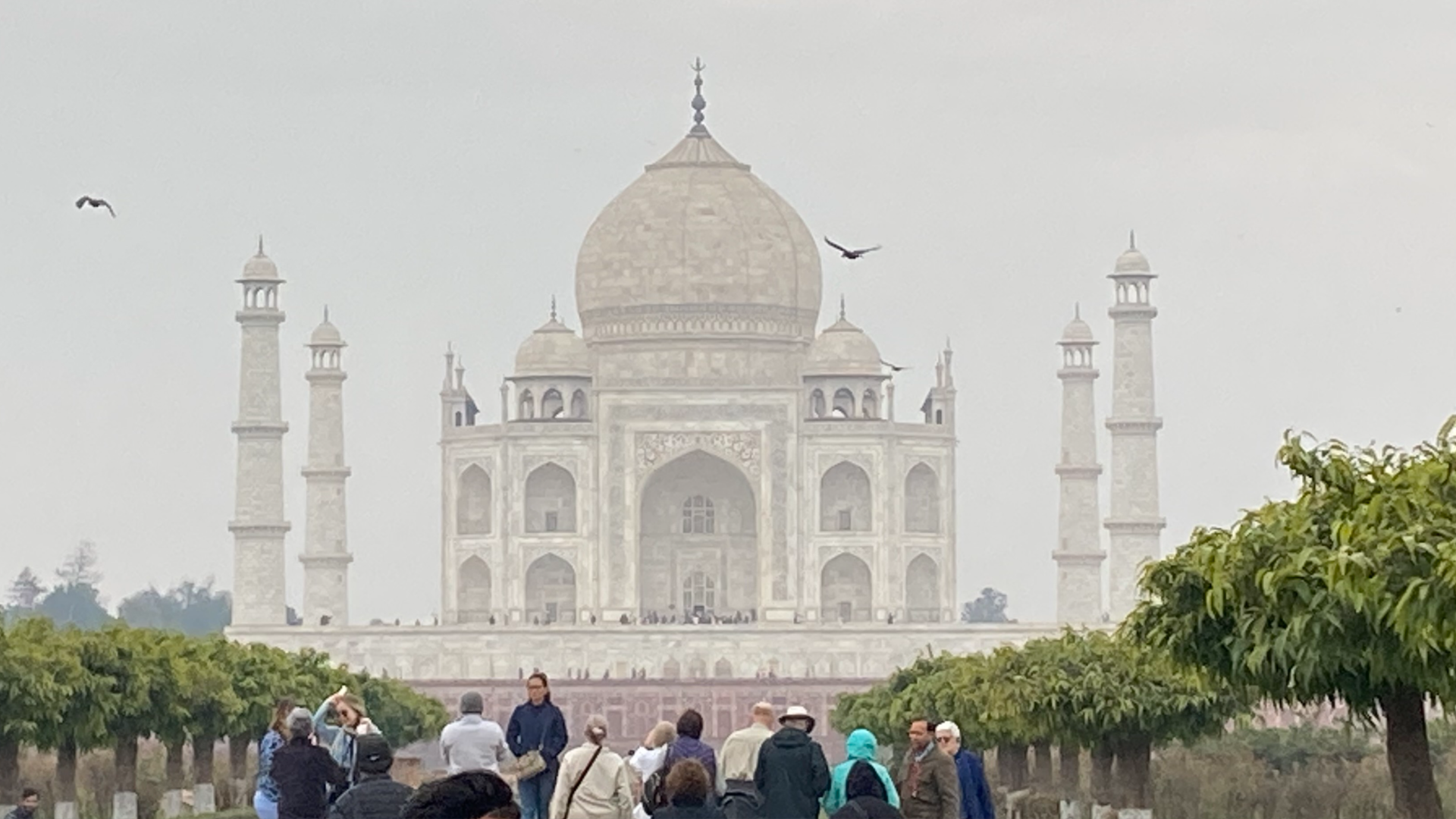 The Taj Mahal in the distance with people and trees closer to the camera.
