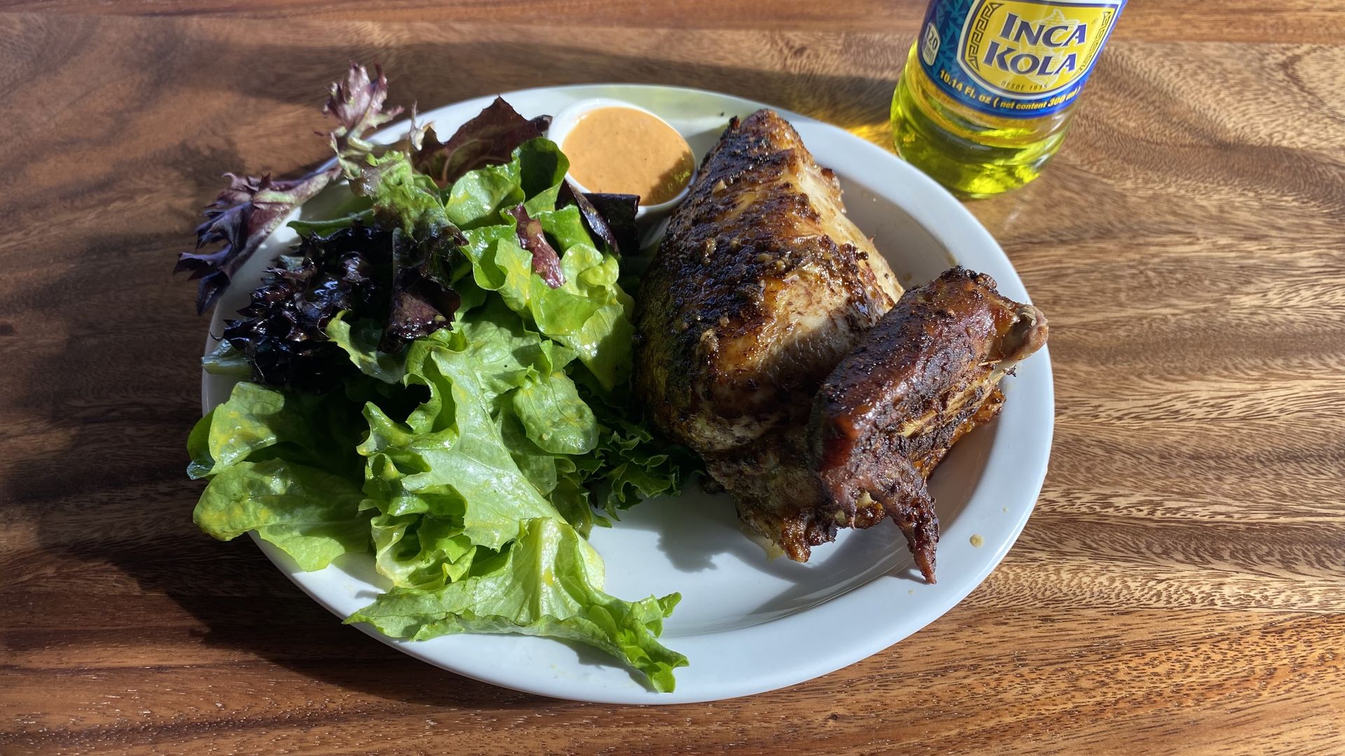 A quarter grilled chicken and salad on a plate, next to a bottle of Inca Kola. 