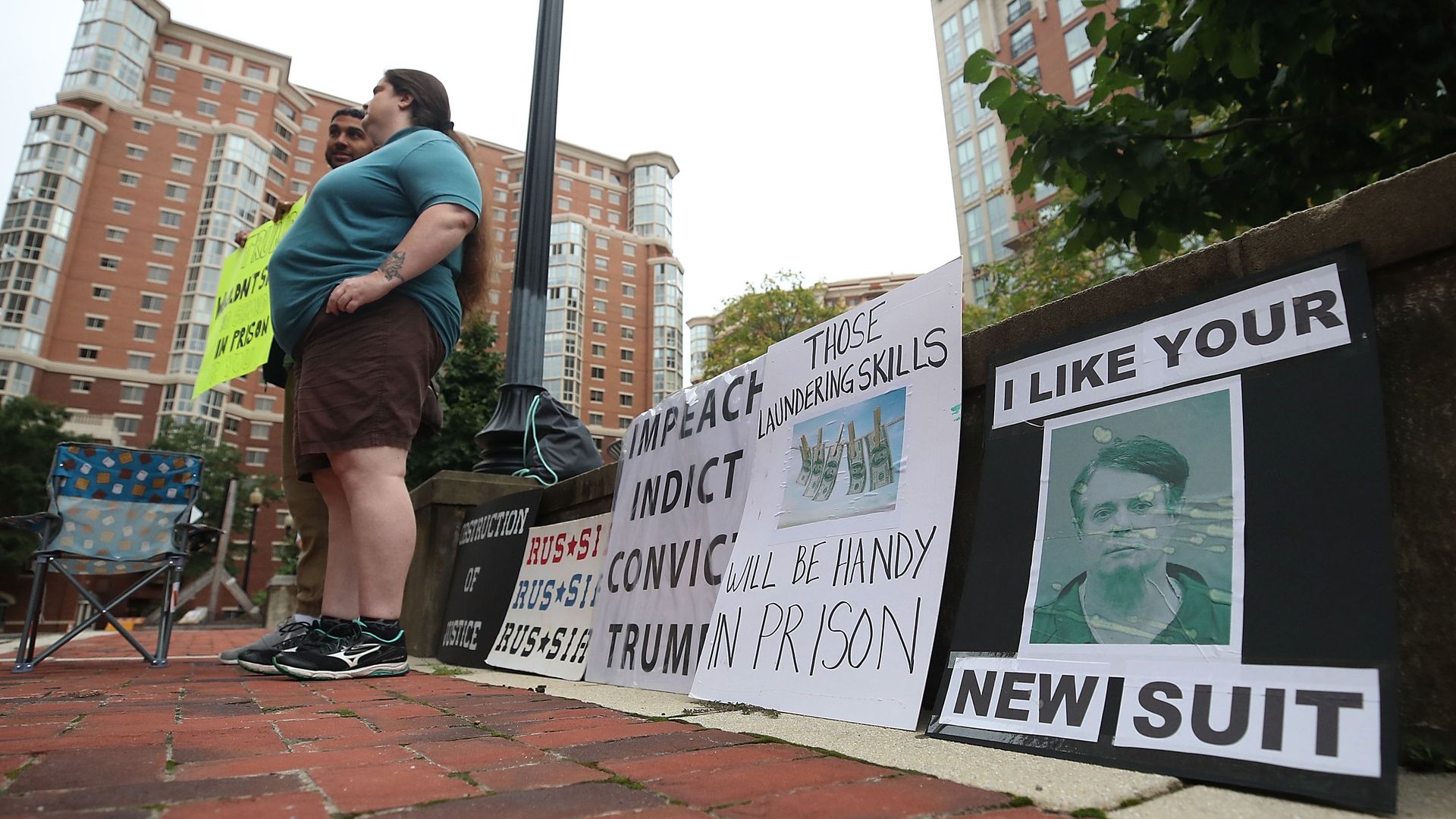 A sign next to protestors with a mugshot of Paul Manafort, that reads "I like your new suit."