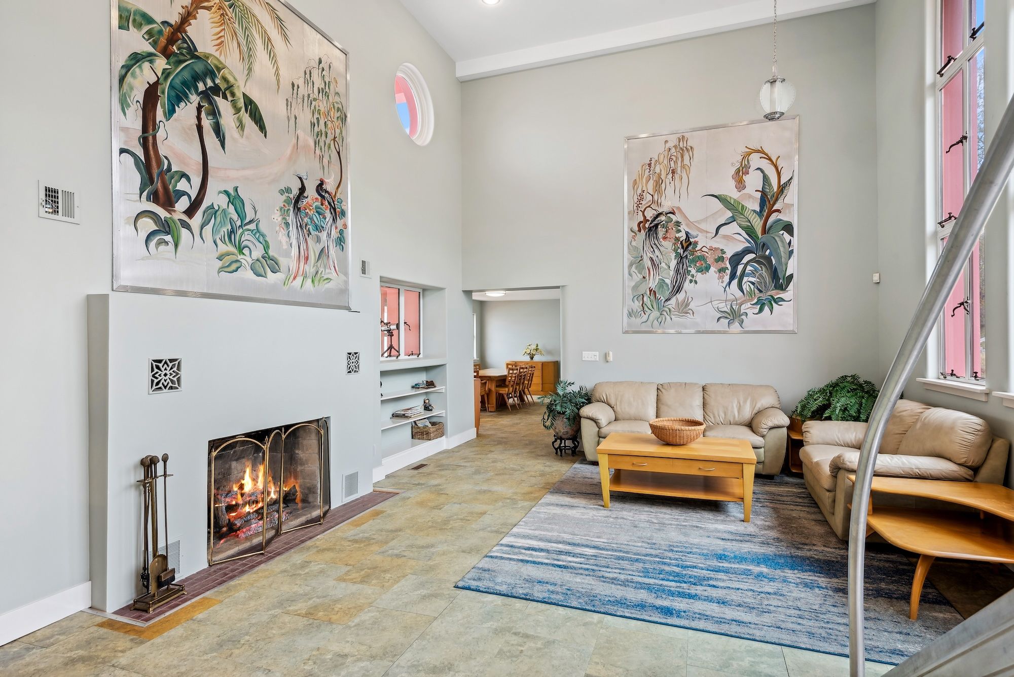 High ceiling room with fireplace and large picture of tropical scene.