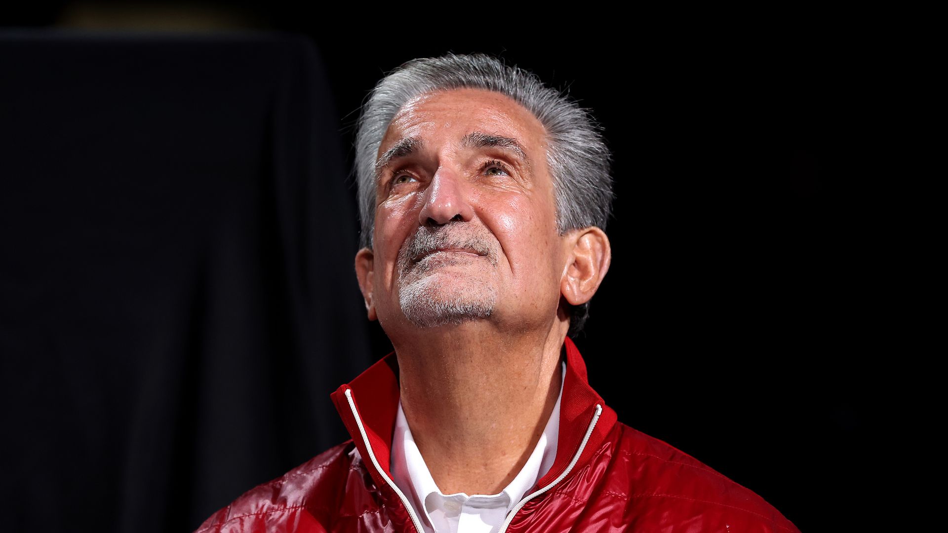 Ted Leonsis in a red jacket looking up against a black background 