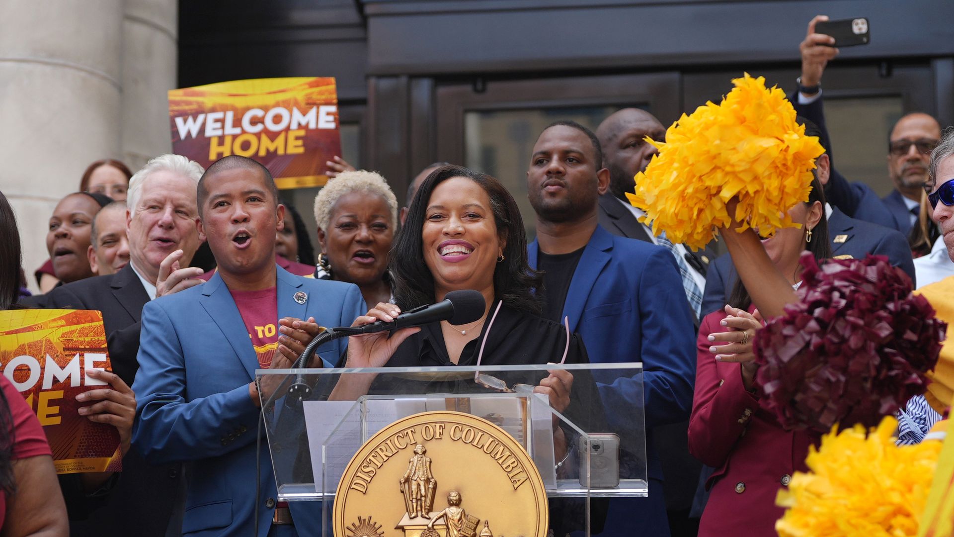 Mayor Muriel Bowser stands at a podium outside of the John Wilson Building as supporters cheer during a rally.