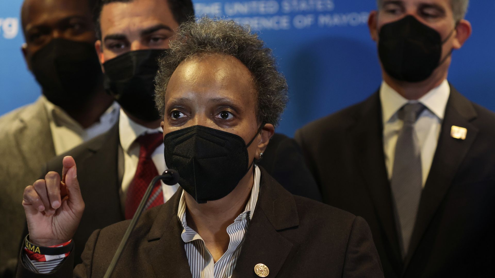 A photo of a masked woman speaking at a podium. 