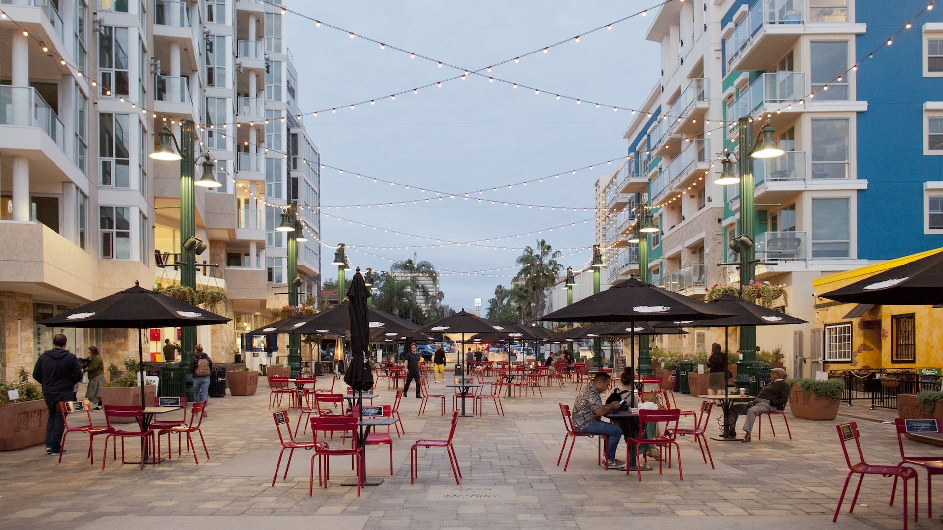 People enjoy patio dining on a plaza lined with apartment buildings in San Diego's Little Italy neighborhood.