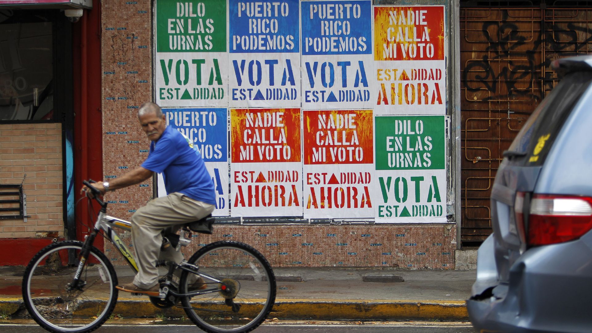 A man on a bicycle rides past six posters urging Puerto Rico's voters to go to the polls and vote on the island's status.