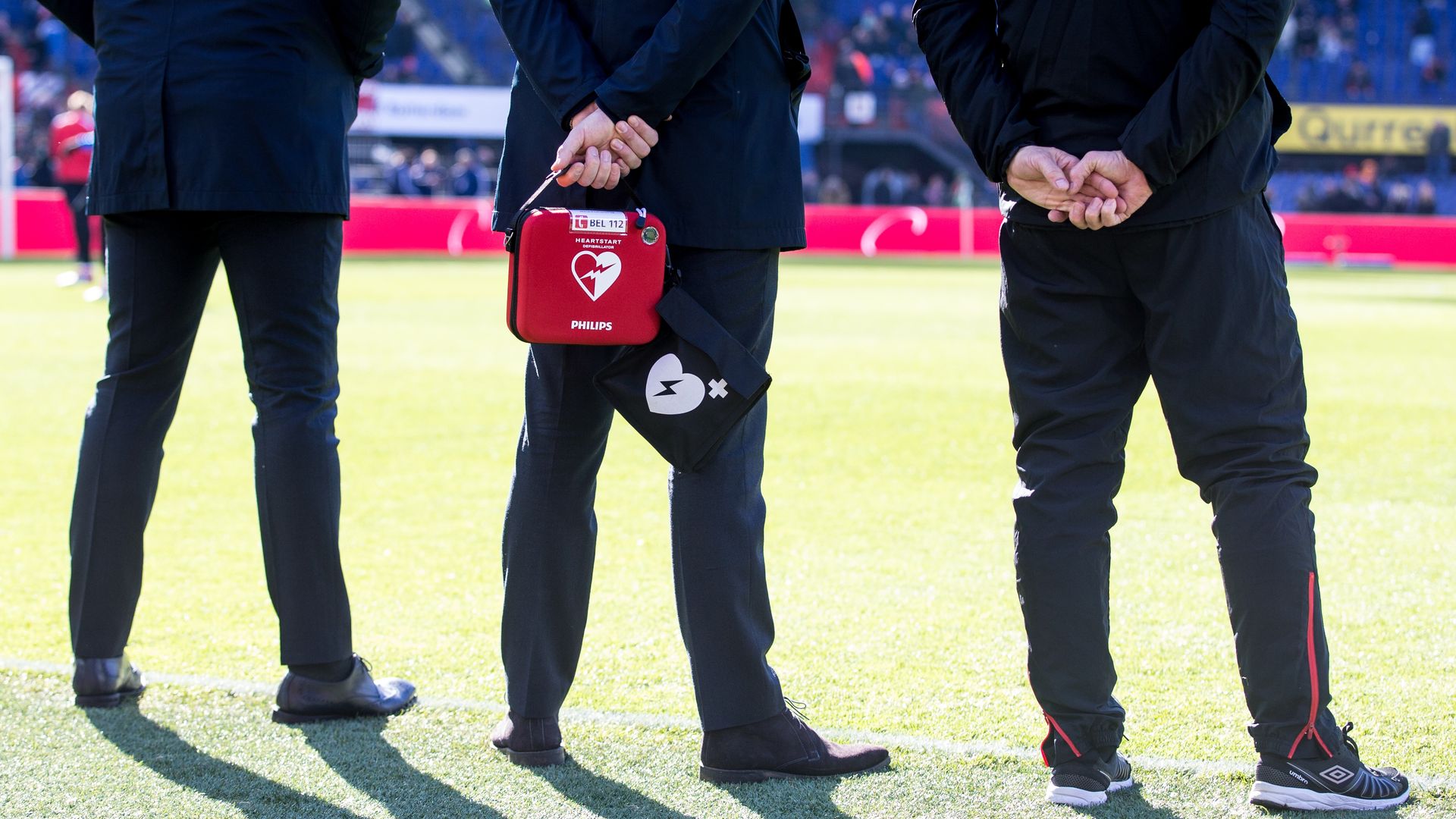 A photo of a person holding a defibrilator standing on a soccer pitch