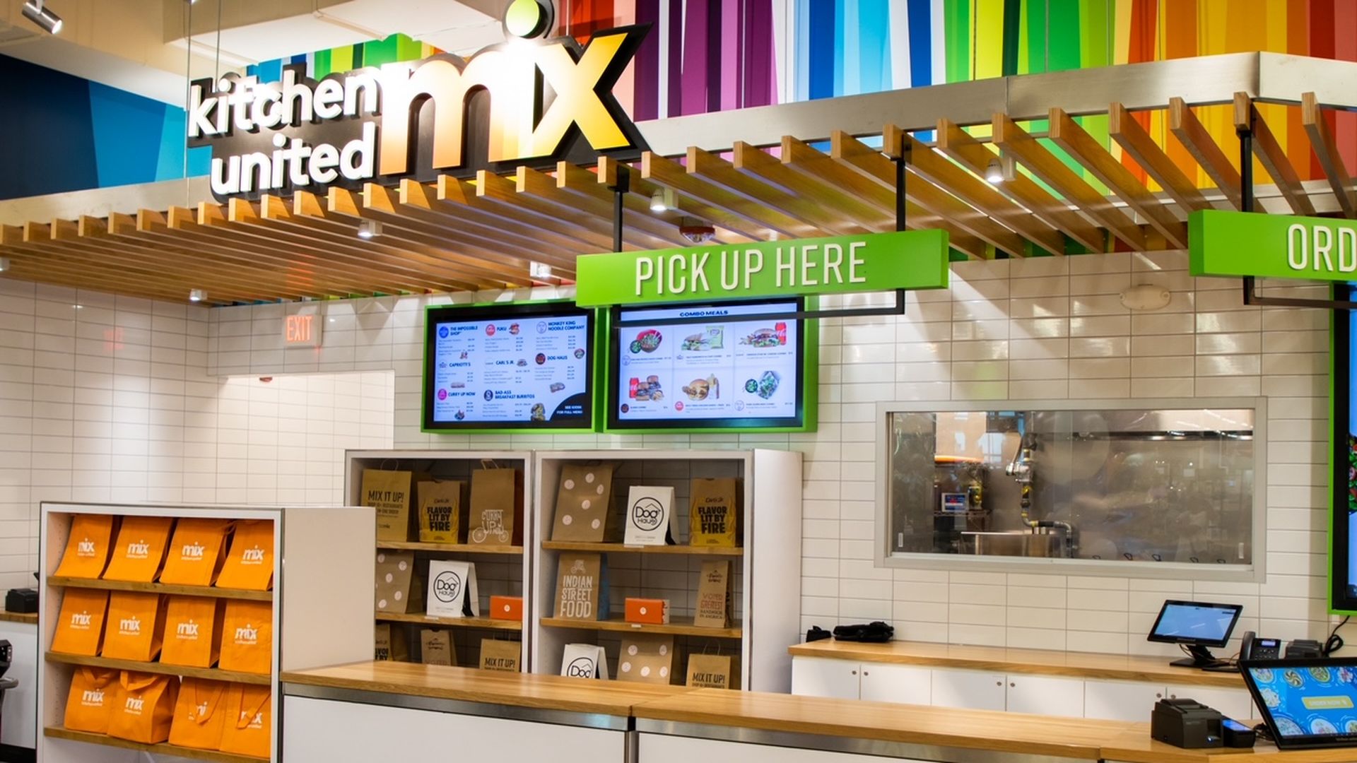 A kiosk in a grocery store with a white checkout desk out front, refrigerated display cases behind and a Kitchen United sign above.