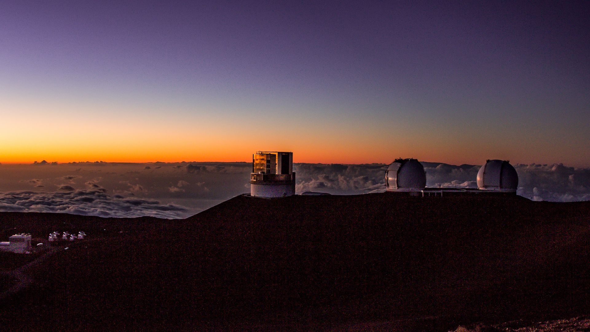 Three telescopes sit atop a mountain at sunset