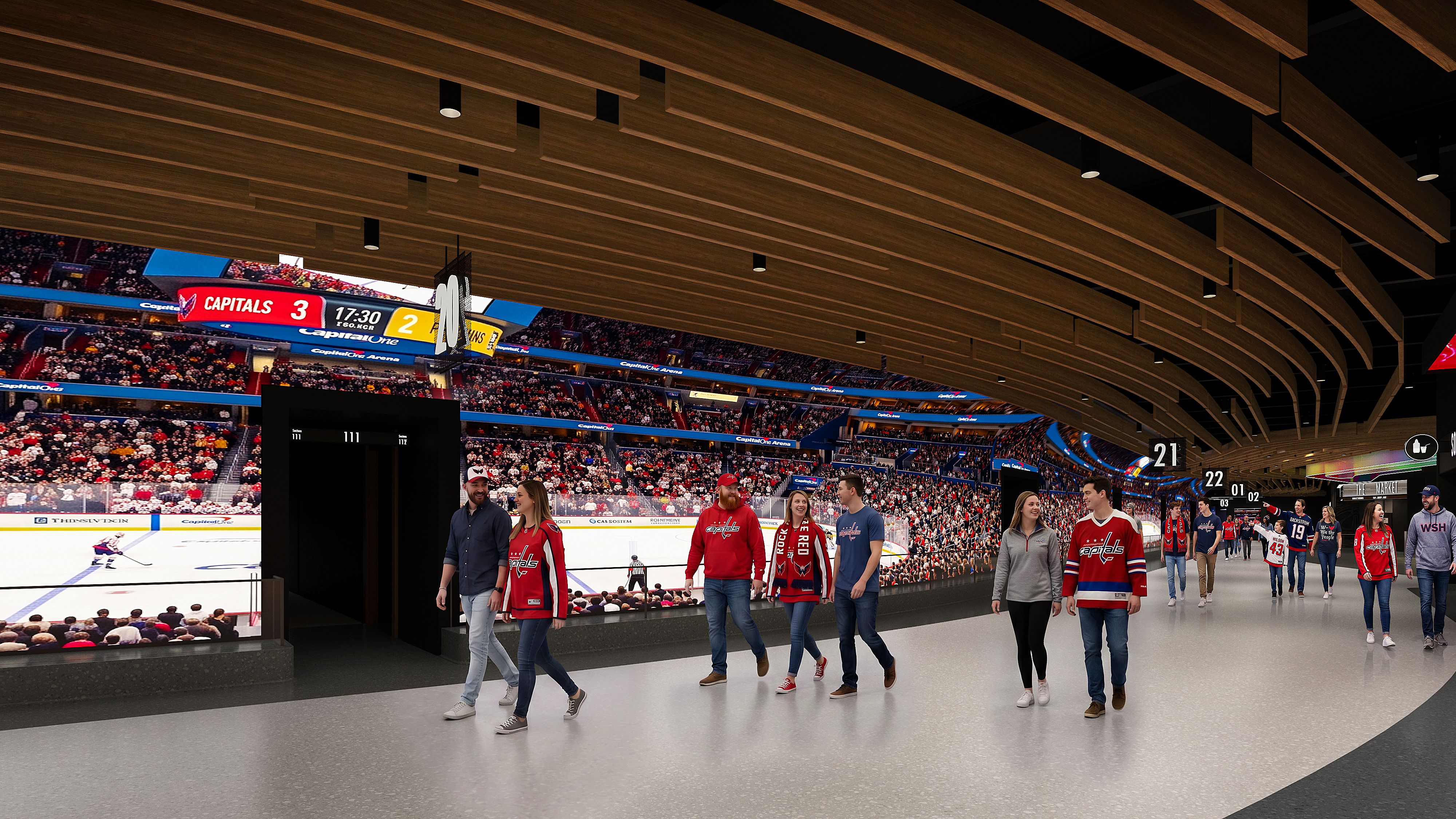 Indoor hockey arena concourse with a brown wood slat ceiling; crowd in stands, players in red Capitals jerseys walk along the rink while a scoreboard shows Capitals 3, opponent 2.
