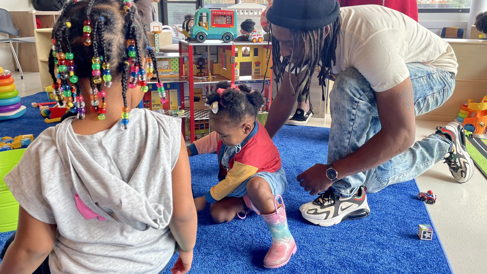 Two children and a caregiver play in a brightly-colored indoor play space. 