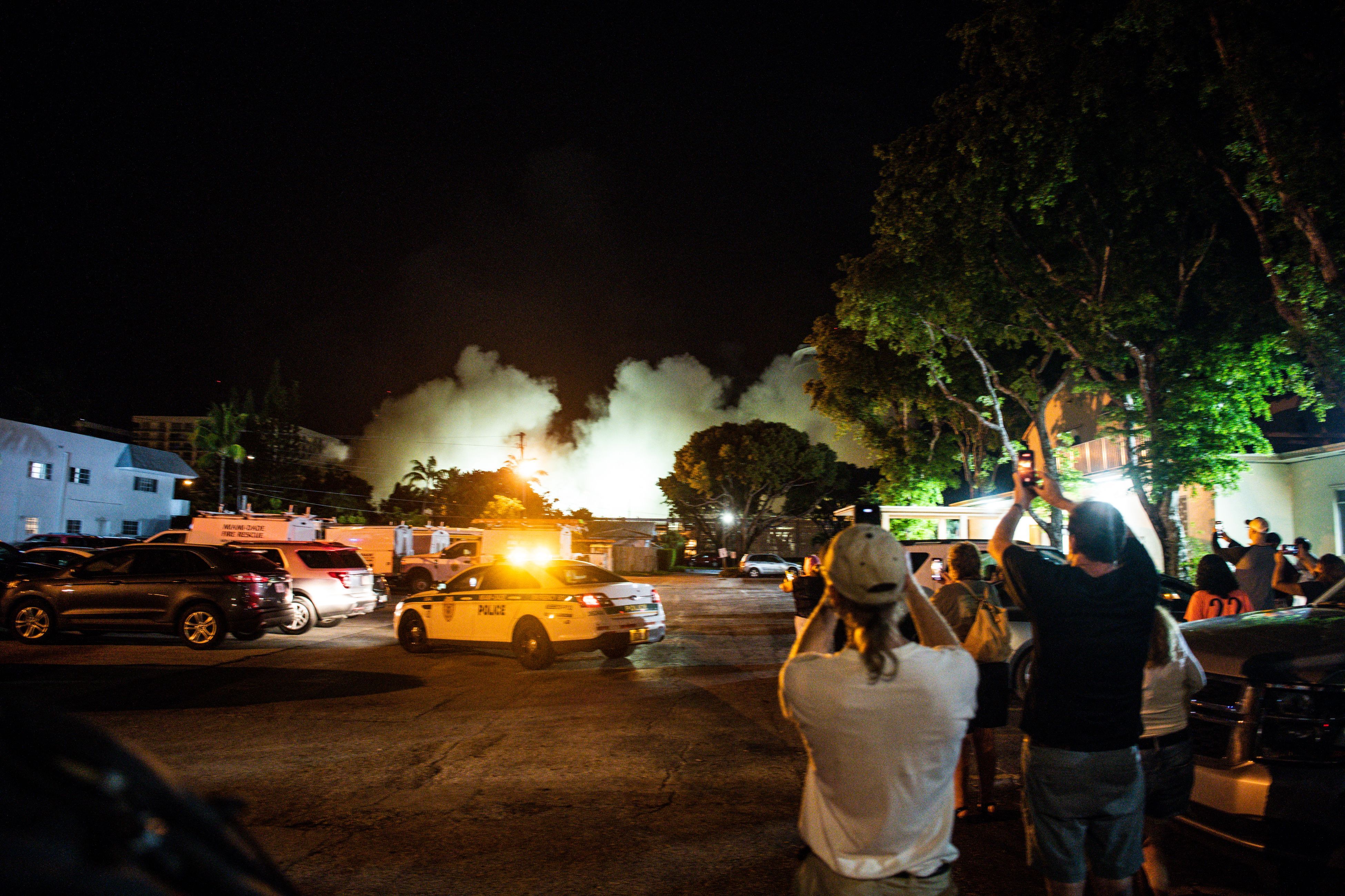 People watch a cloud of dust after the rest of the Champlain South tower was demolished by a controlled explosion in Surfside, Florida, north of Miami Beach, late on July 4