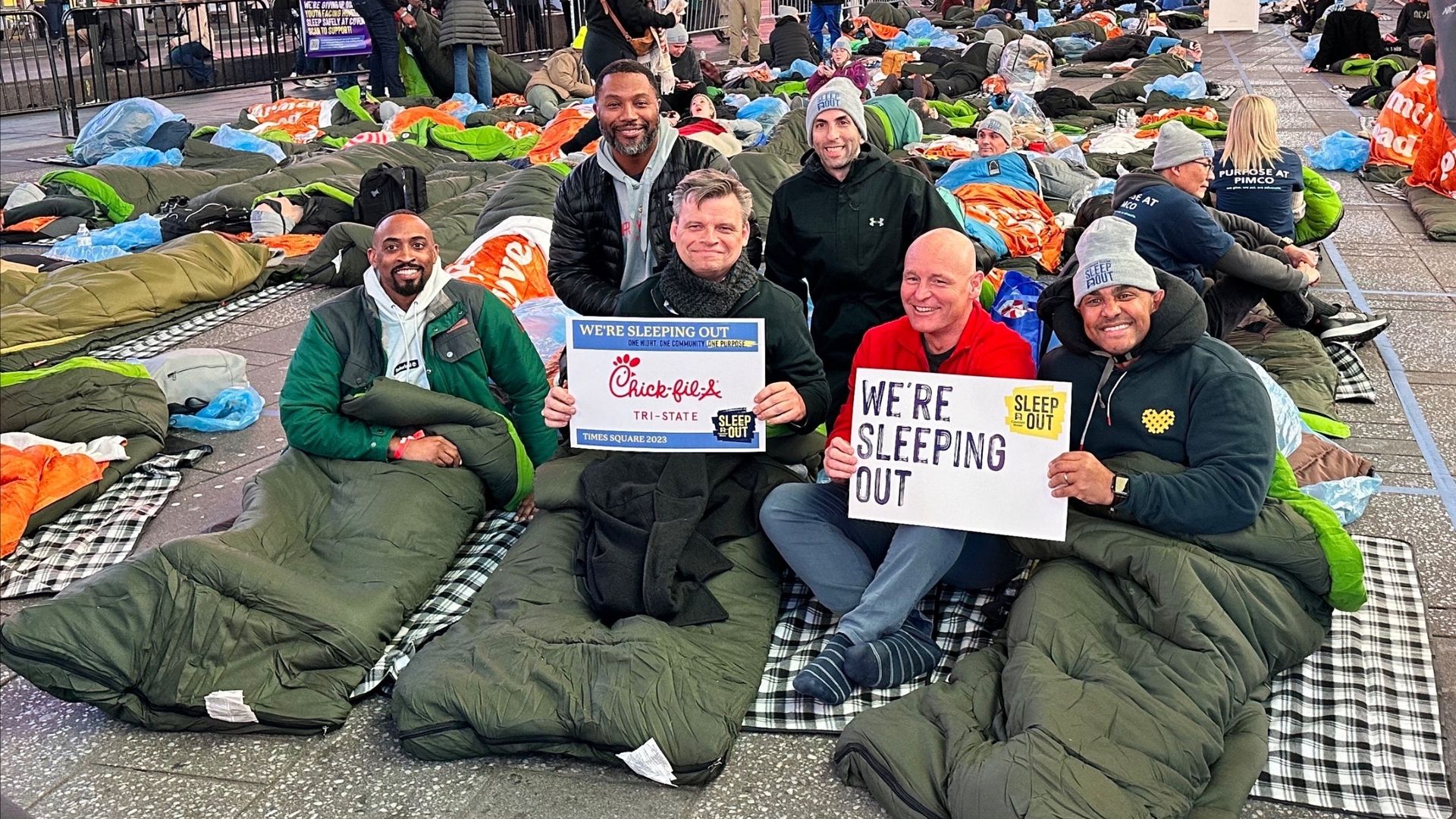 Participants holding signs and sleeping bags in Times Square for an overnight charity event supporting homelessness awareness.