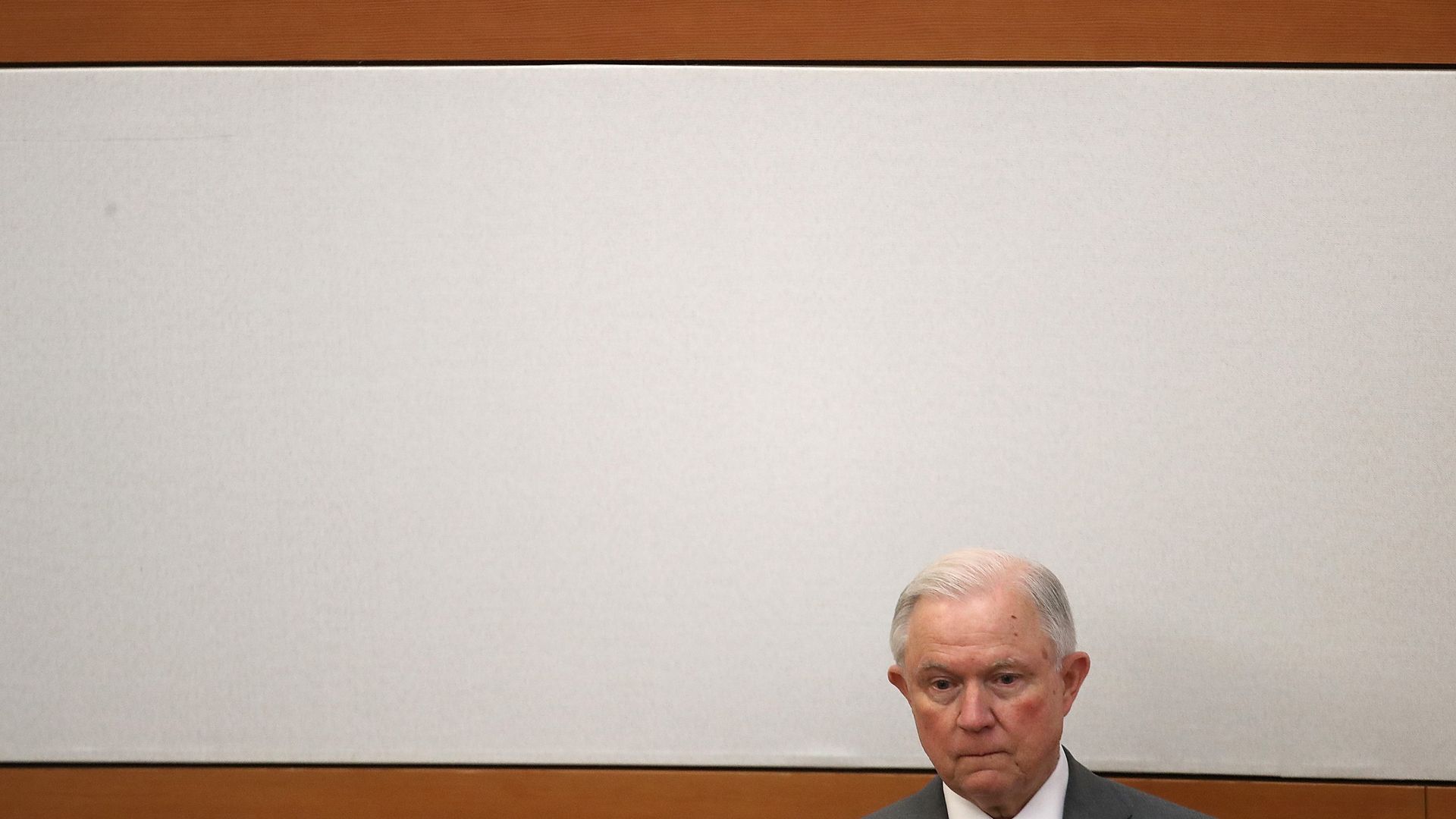 Attorney General Jeff Sessions' head at the bottom right side of the photograph with a wall with wooden, horizontal planks in the background. 