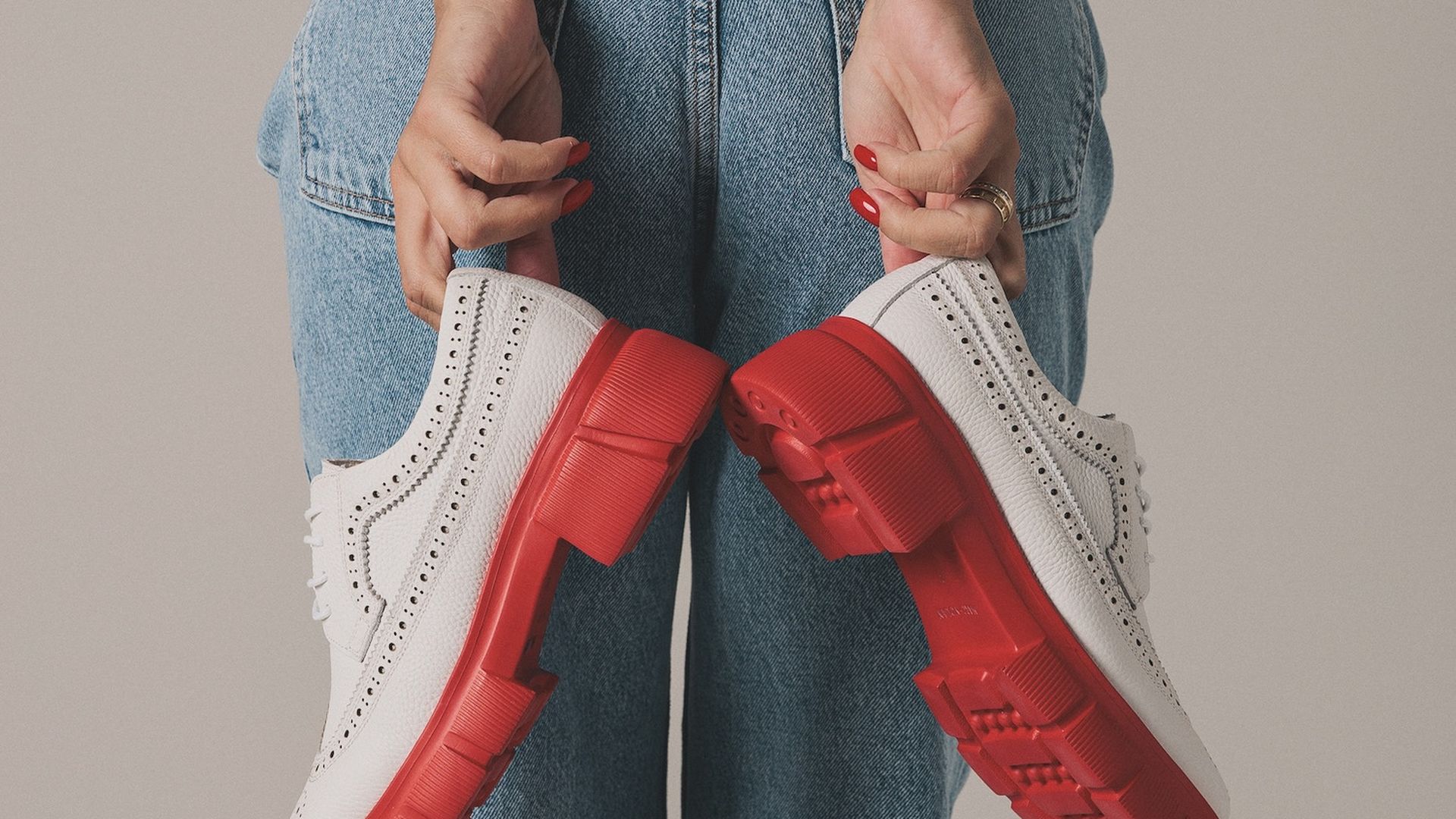 Back of person in jeans holding white and red oxford shoes.