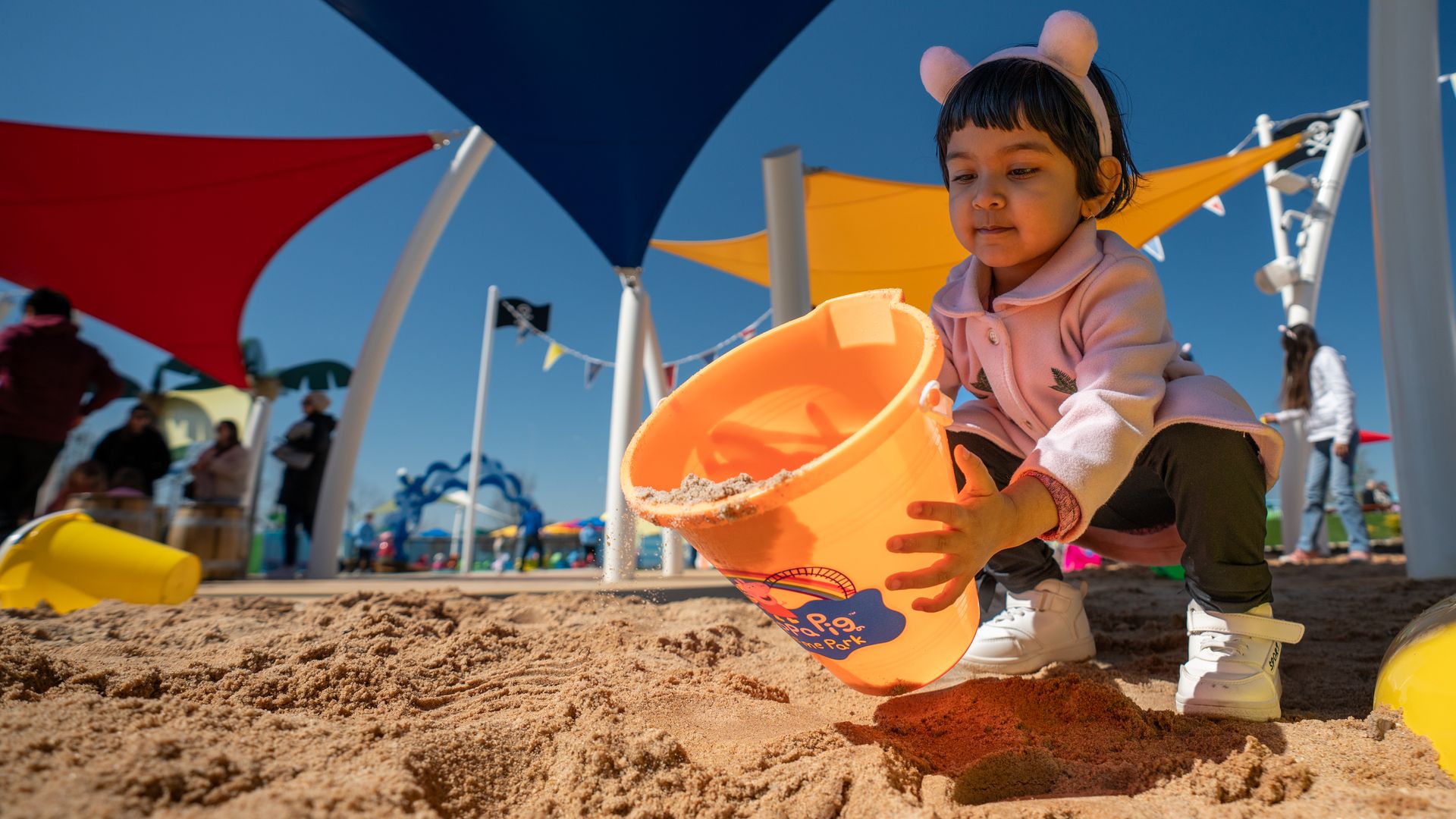 A girl uses a bucket to scoop up sand