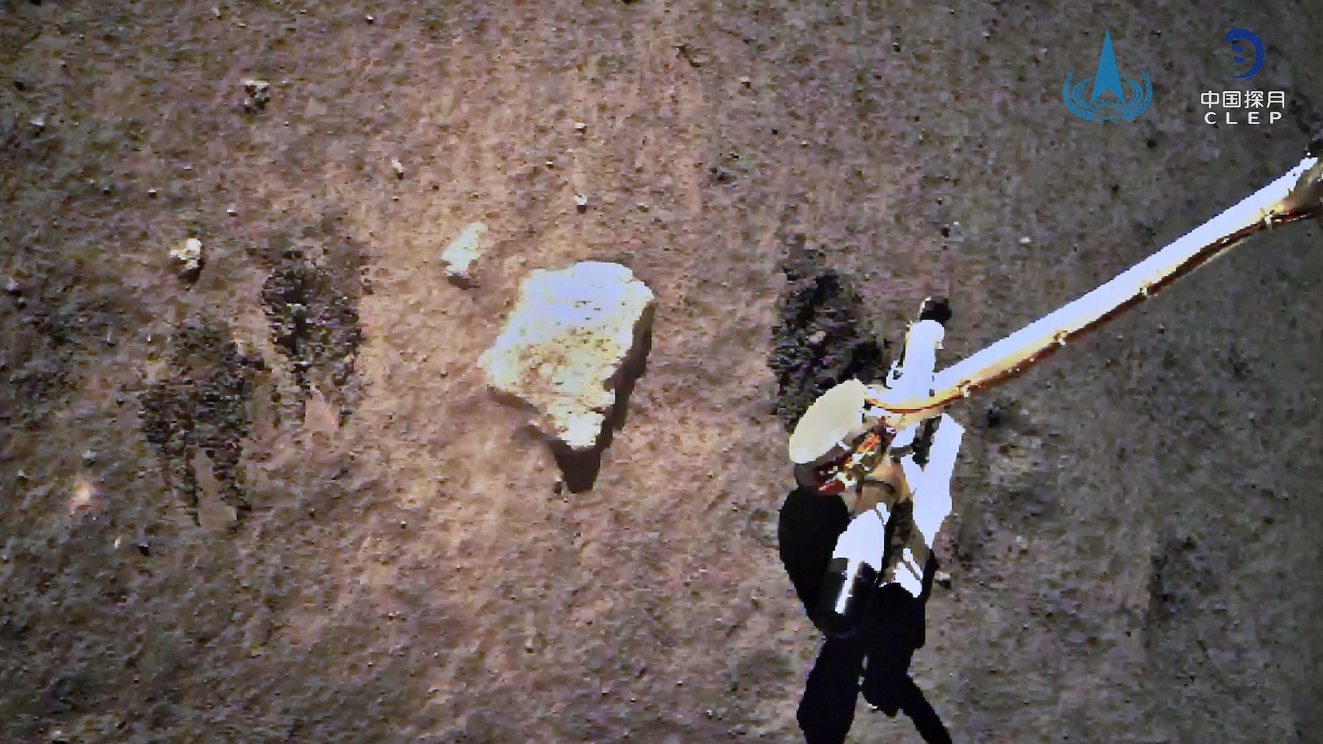 The arm of a spacecraft extends into the lunar dirt to gather a sample of Moon rocks for China