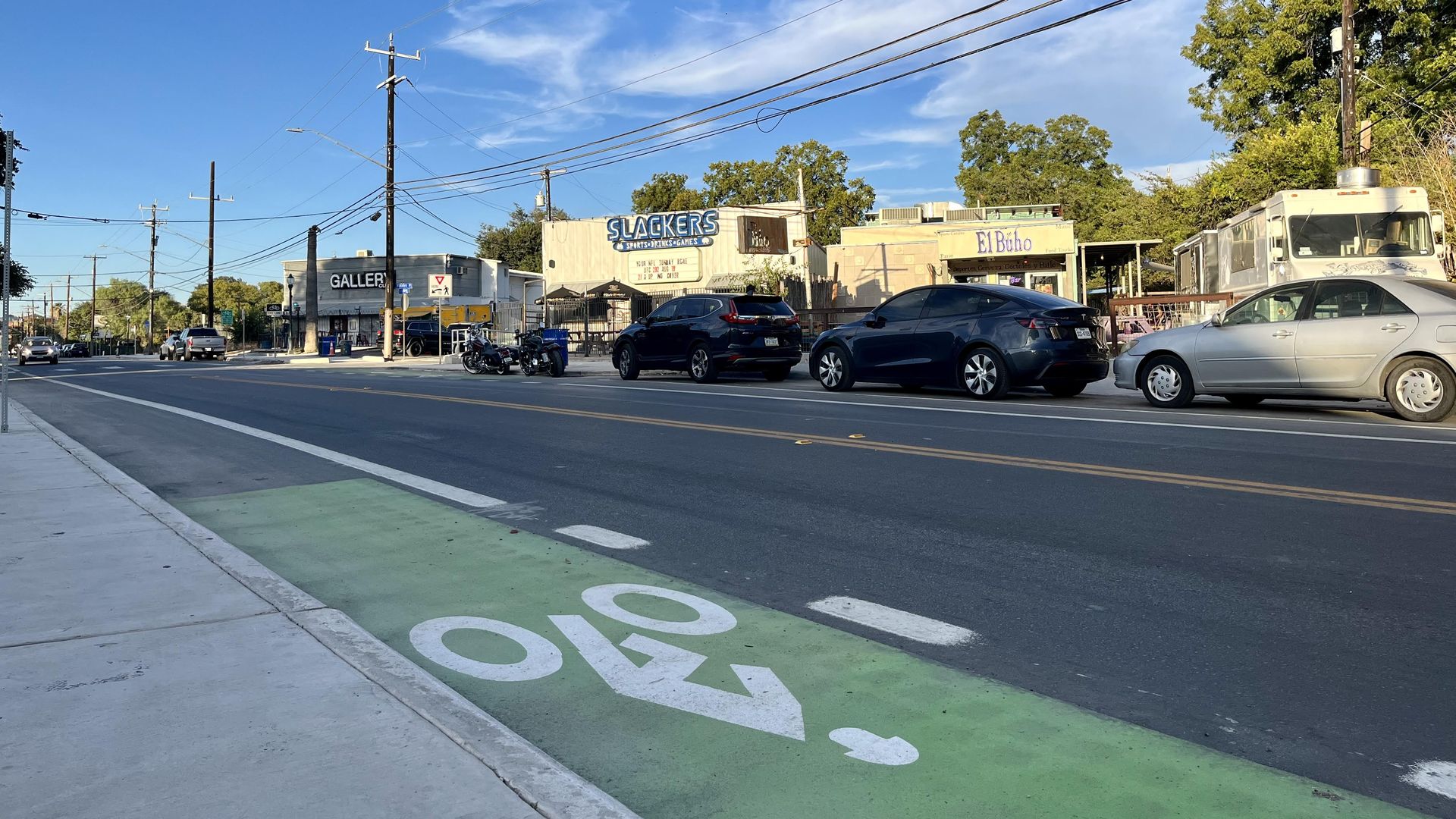 A newly paved street and bike lane in front of bars and on-street parking.