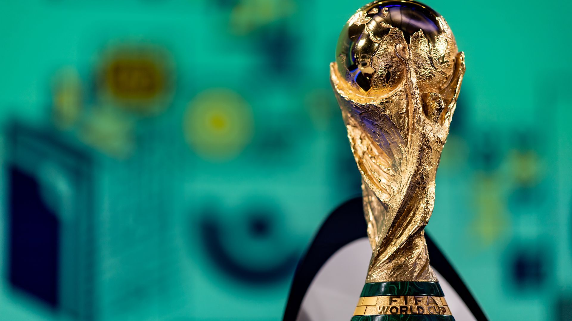 The gold FIFA World Cup trophy with green background behind it. 