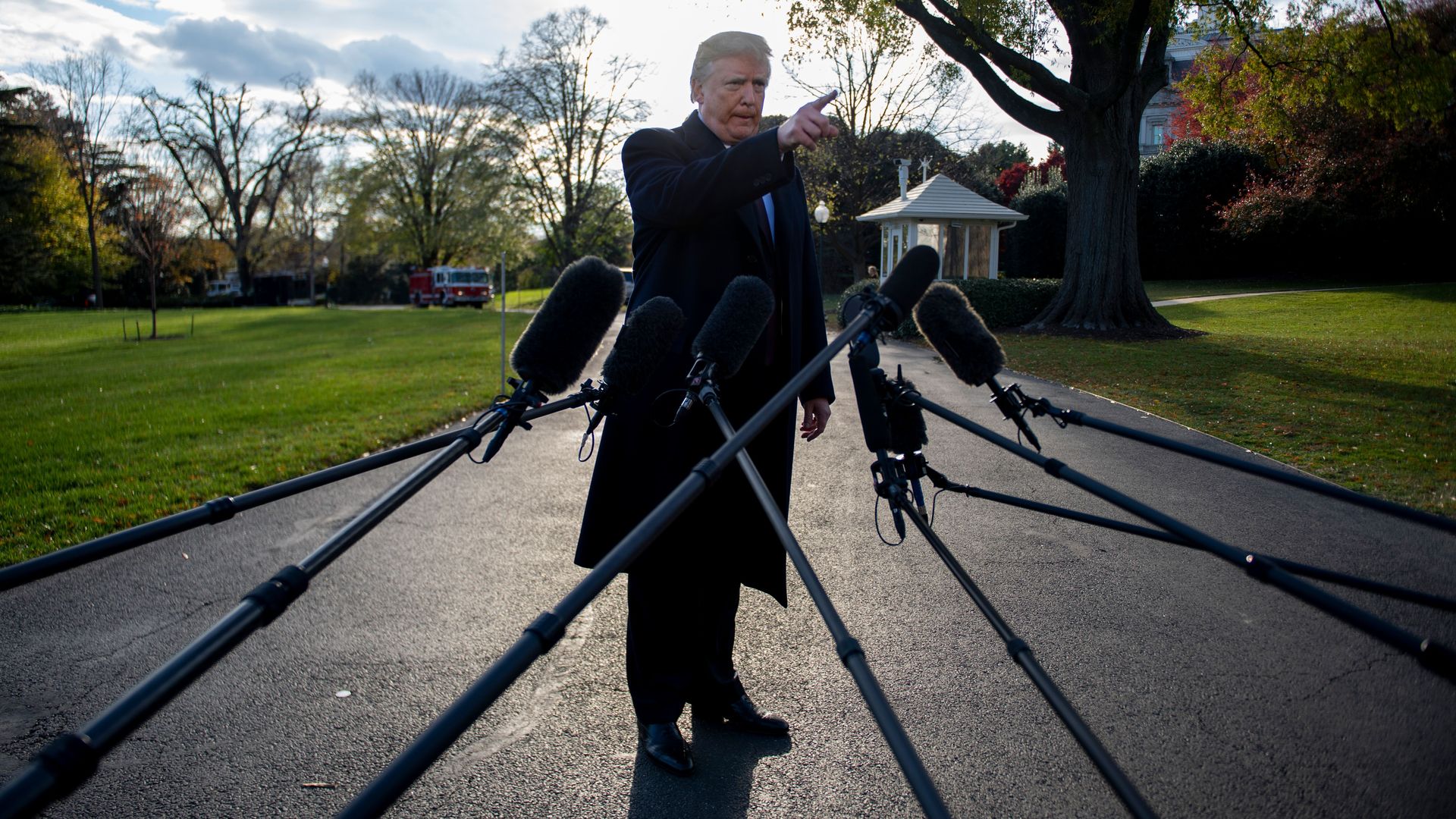 Donald Trump pointing toward the camera where reporters are standing on the lawn outside the White House. There are microphones reaching out from the angle of the camera. 