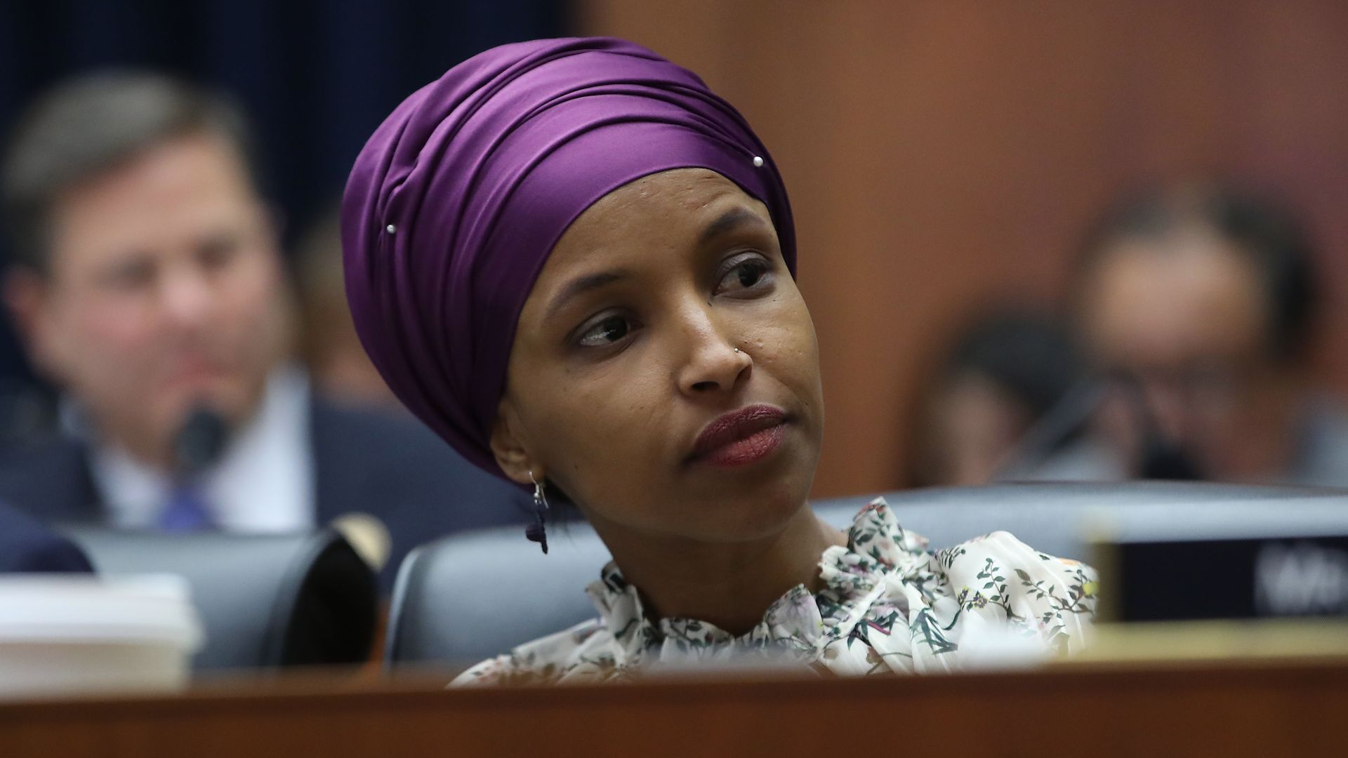 In this image, Ilhan Omar sits behind a placard with her name on it. 