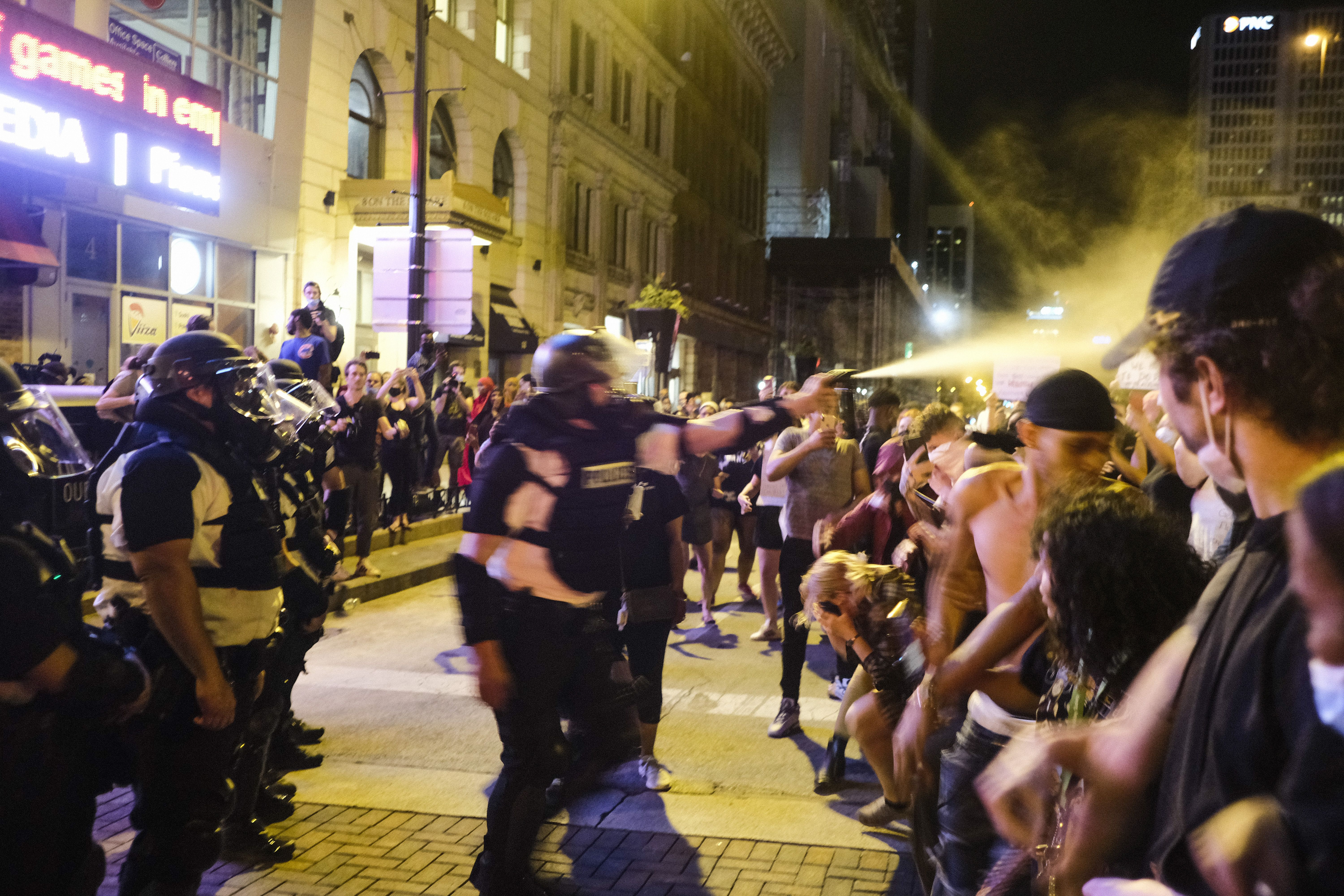 Columbus police officers clash with protestors on a street, with an officer spraying something into a row of people. 