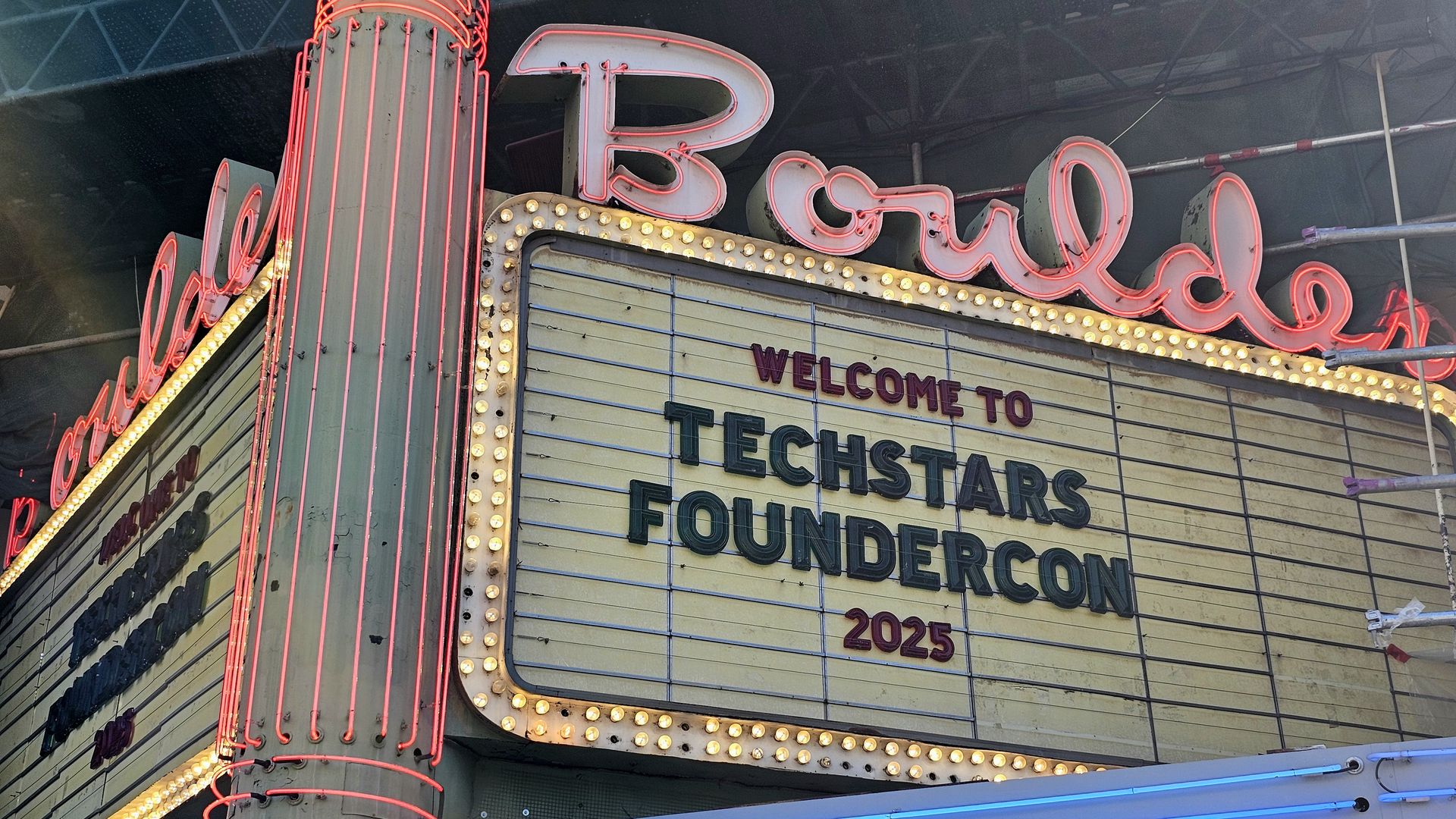 Vintage theater marquee with red neon lights spelling "Boulder" and a sign reading "Welcome to Techstars FounderCon 2025" in black and red letters on a yellow background.