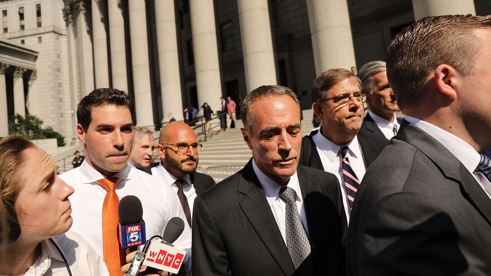 Chris Collins walks out of court with media holding microphones near him.