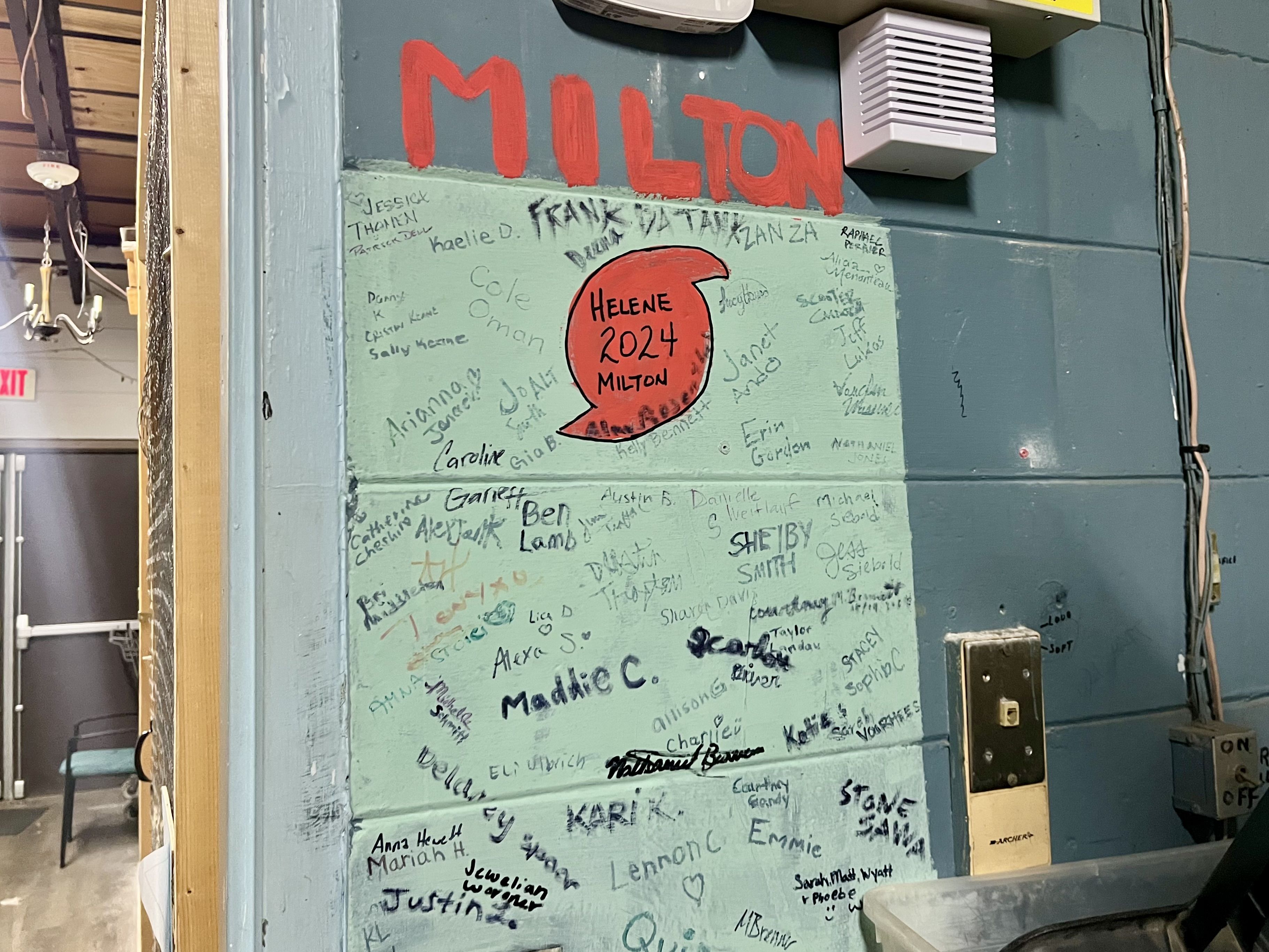 A wall painted with a red cyclone symbol that says "Helene 2024 Milton."