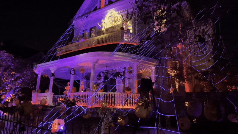 A house is decorated for Halloween with lights, pumpkins and skeletons.