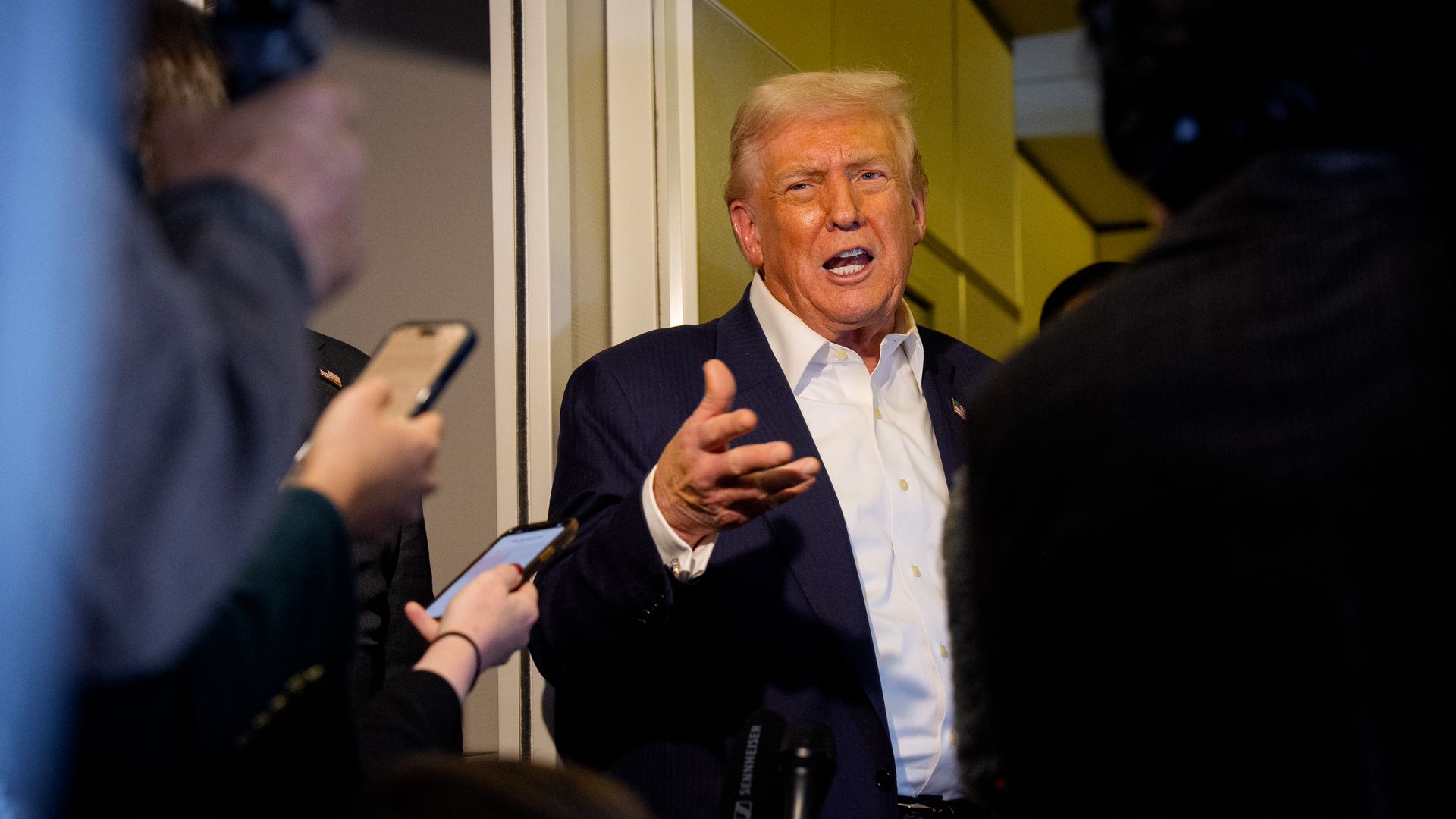 Trump, wearing a blue suit jacket and white shirt talking to reporters