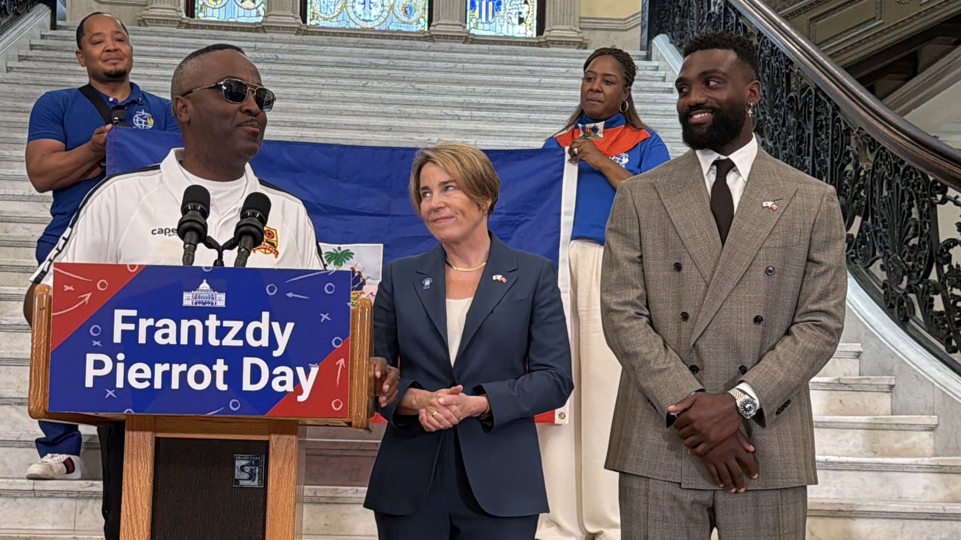 From left, coach Corlton Simmonds, Gov. Maura Healey and Melrose High School alumnus and Haitian Men's Soccer Team player Frantzdy Pierrot stand at a lectern in the Massachusetts State House to commemorate Frantzdy Pierrot Day.