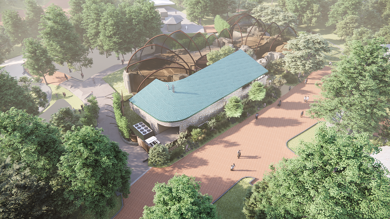 Aerial view of a park showing a turquoise-roofed stone pavilion with curved walls, brown arched metal frames behind it, a red-brick walkway, green trees, and people strolling along paths.