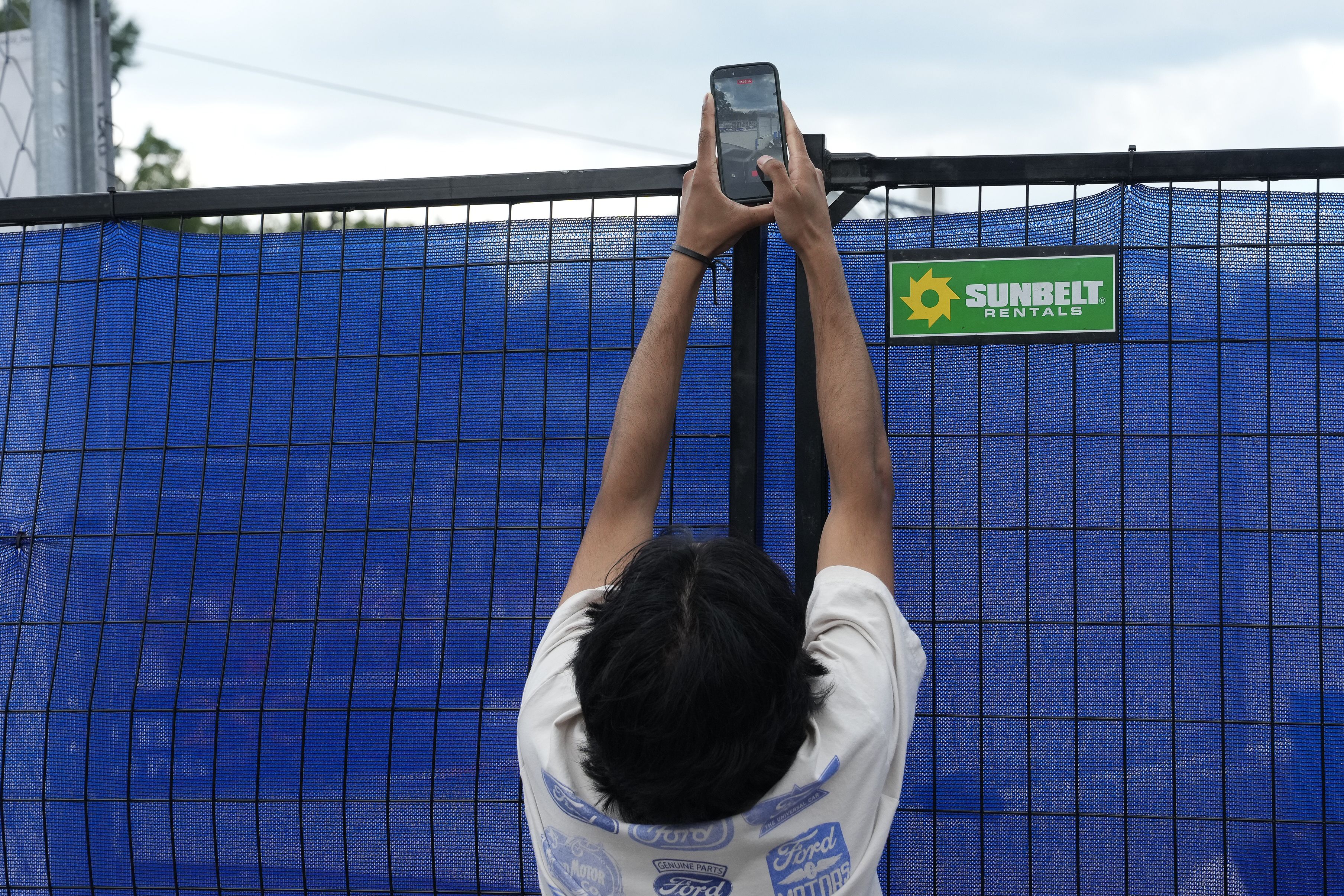 A fan reaches above blue mesh on a fence to film the IndyCar race in D.C.