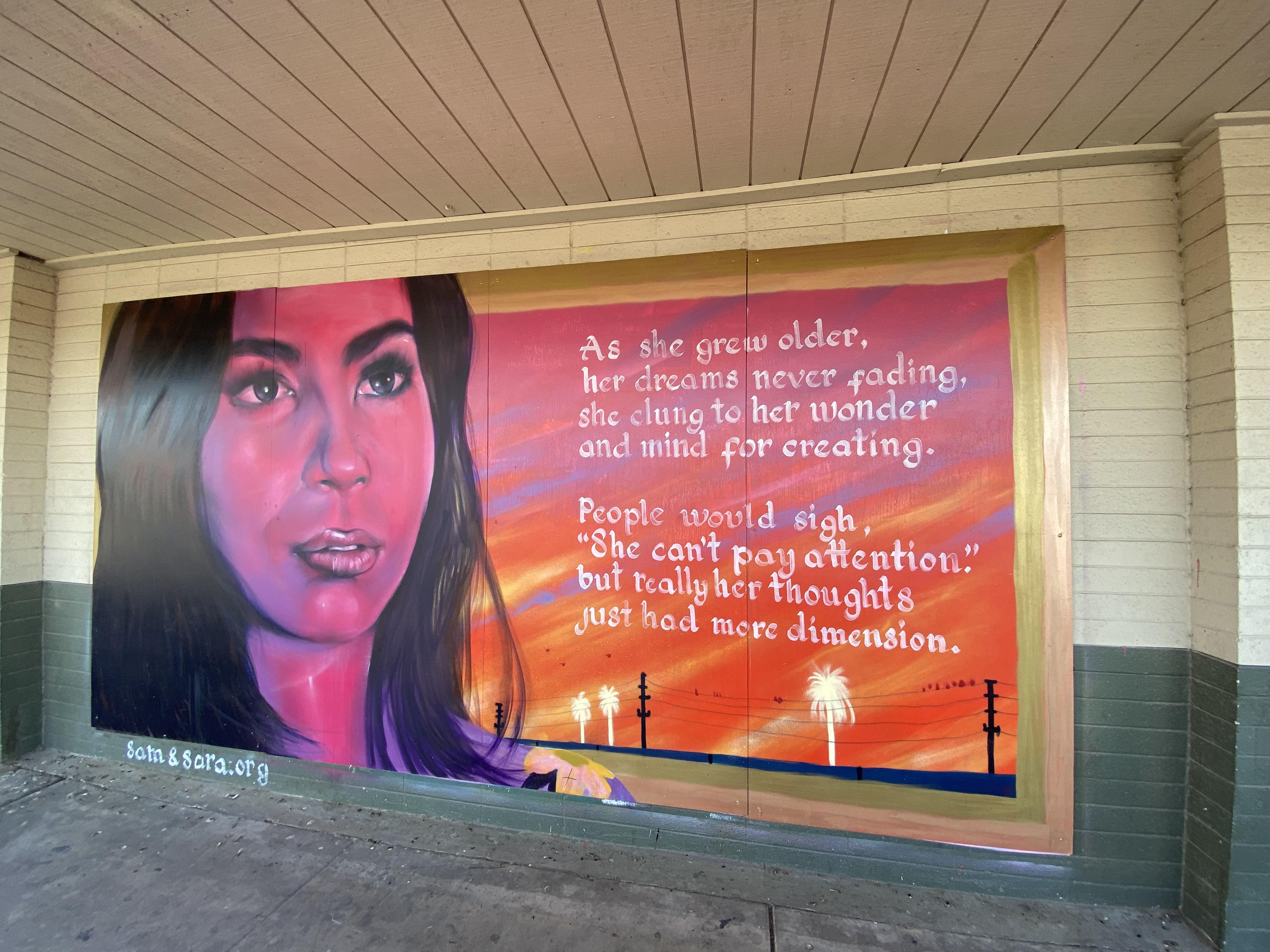 A mural depicting a woman next to an inspirational quote over a red and orange sky. 