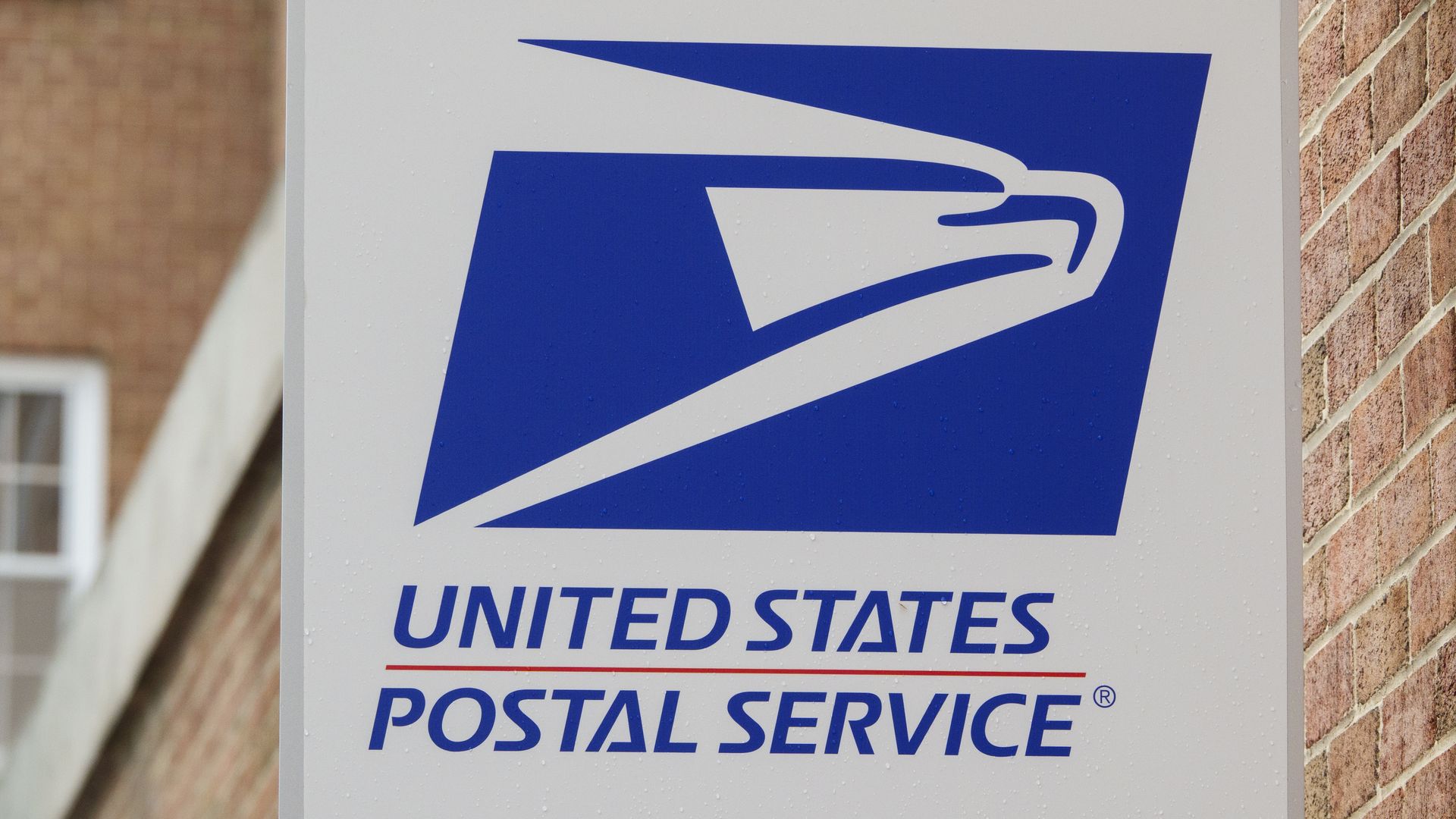 The United States Postal Service logo on a sign attached to a brick building. 