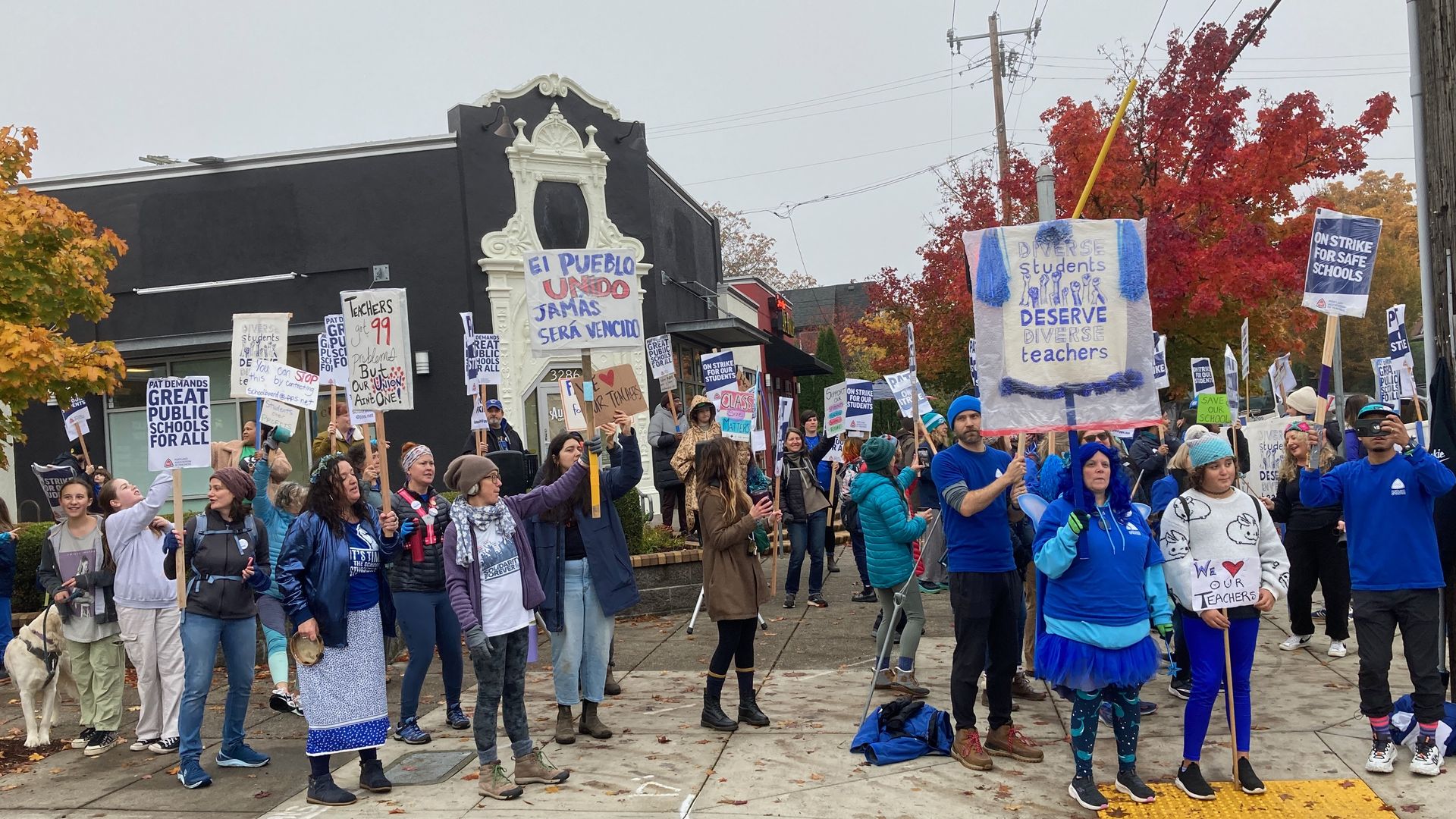 Teachers and supporters hold strike signs on a street corner.