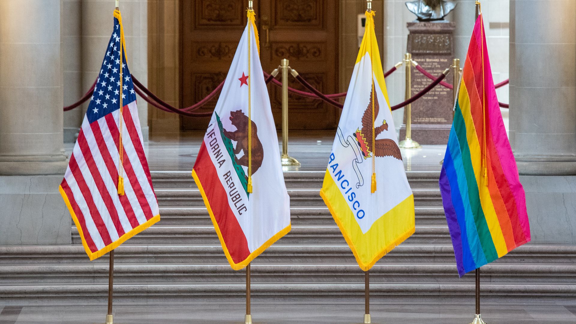 Photo of the U.S. flag, California flag, San Francisco flag and LGBTQ Pride flag standing in a row 