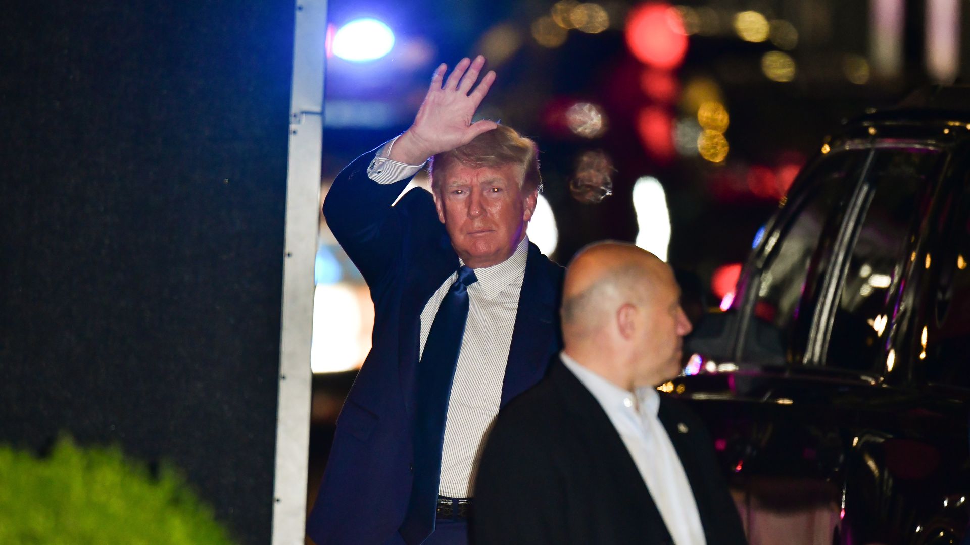 Photo of Donald Trump waving his right hand as he exits a vehicle on a road at night