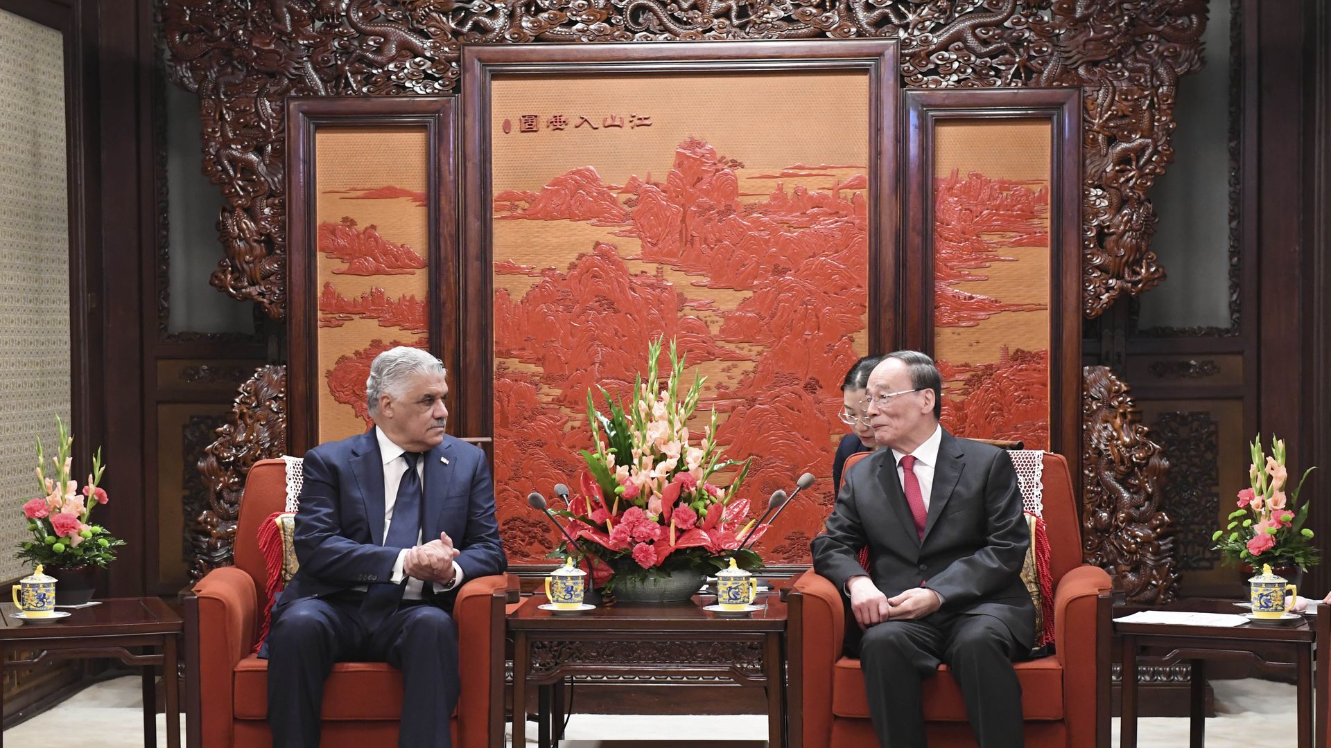 Dominican and Chinese leaders sit on armchairs in front of an orange and red painting