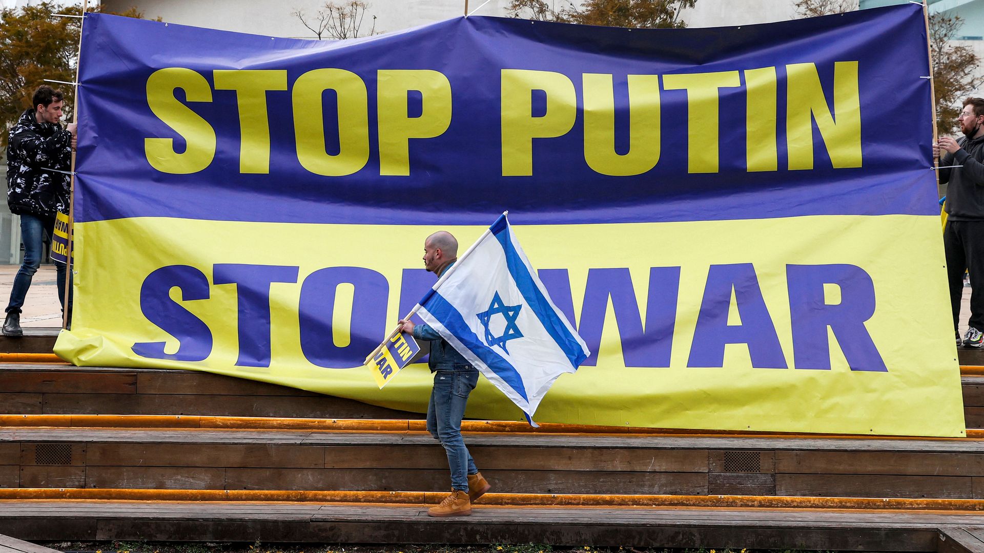 A demonstrator holds up an Israeli flag while standing before an anti-war banner during a protest against Russia's invasion of Ukraine, in Tel Aviv on March 20, 2022.