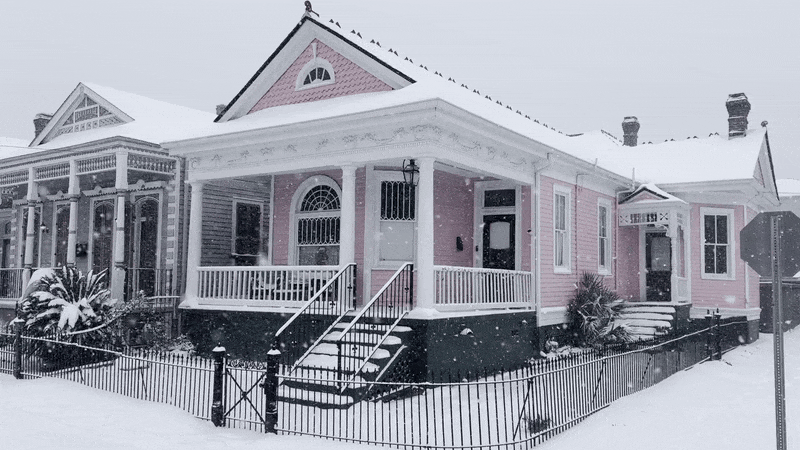 Snow falls on a pink house on a New Orleans street.
