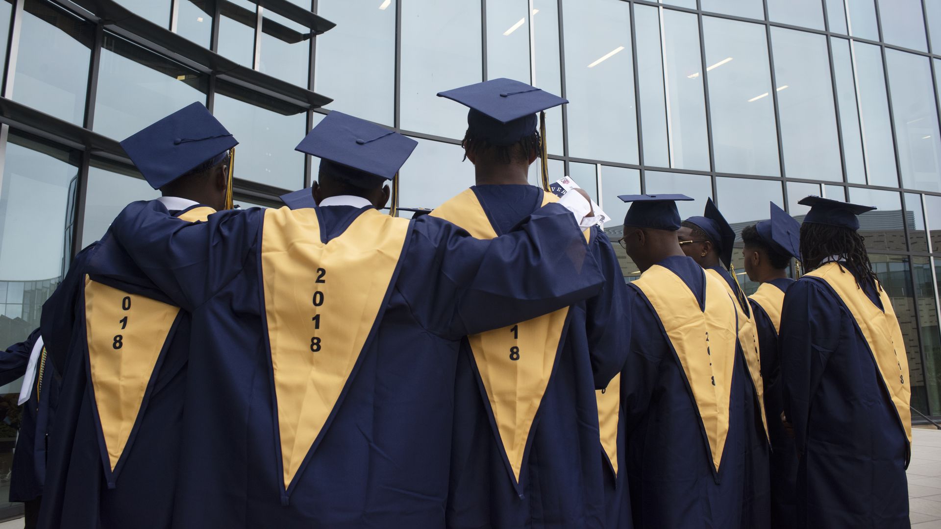 A group of high school graduates with their backs to the camera and their arms over each other's shoulders