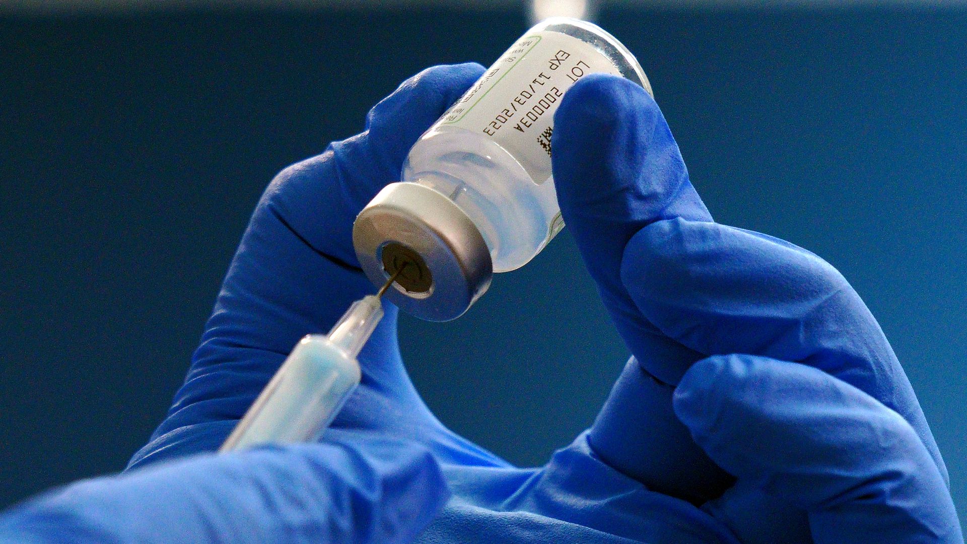 Someone wearing blue gloves pulls a dose of Moderna's COVID-19 vaccine into a needle.