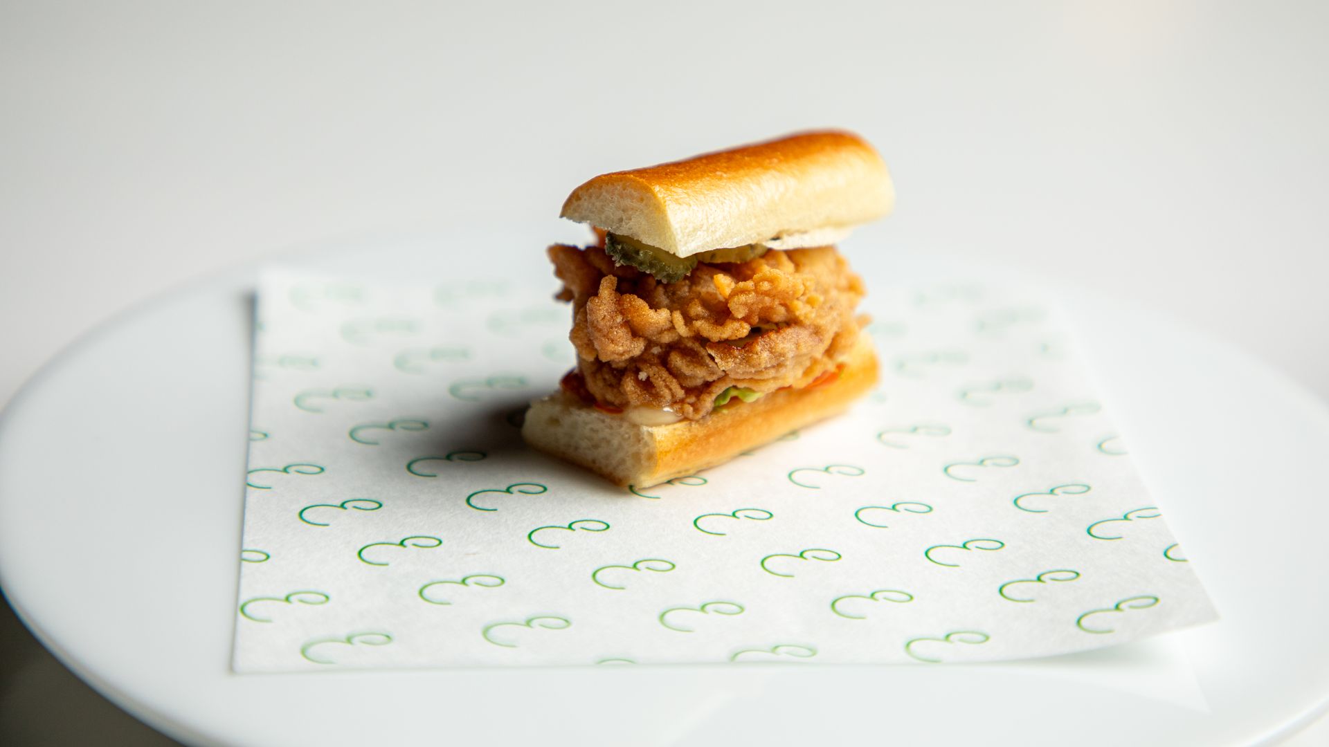 A miniature poboy sits on a tissue paper on a white plate. 