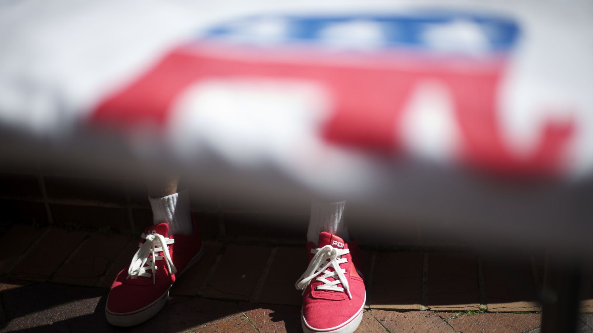 A boy with converse stands under a flag with the GOP elephant on it 