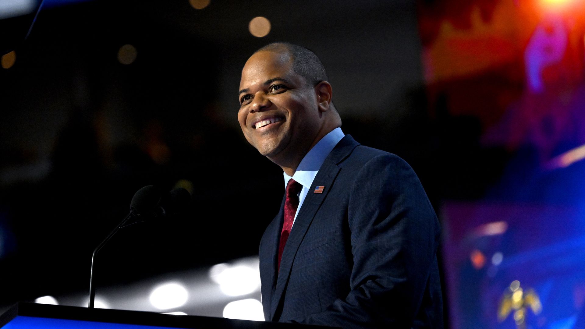 A man wearing a suit looks out over a podium and smiles
