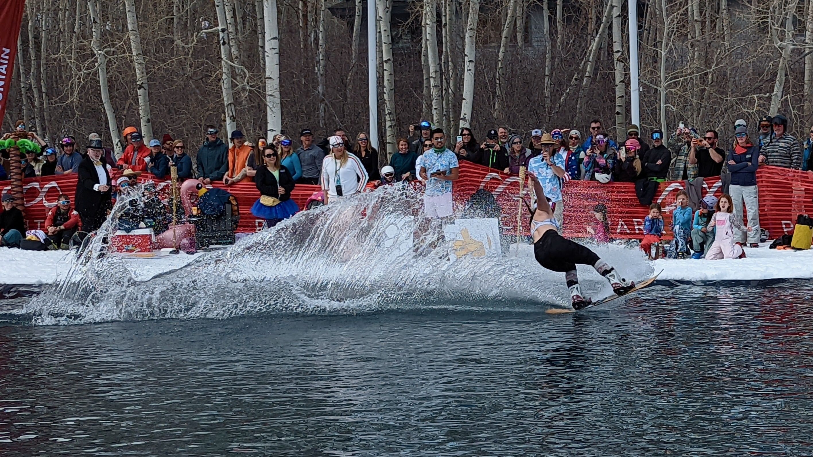 A woman makes a wave as she snowboards onto a pond.