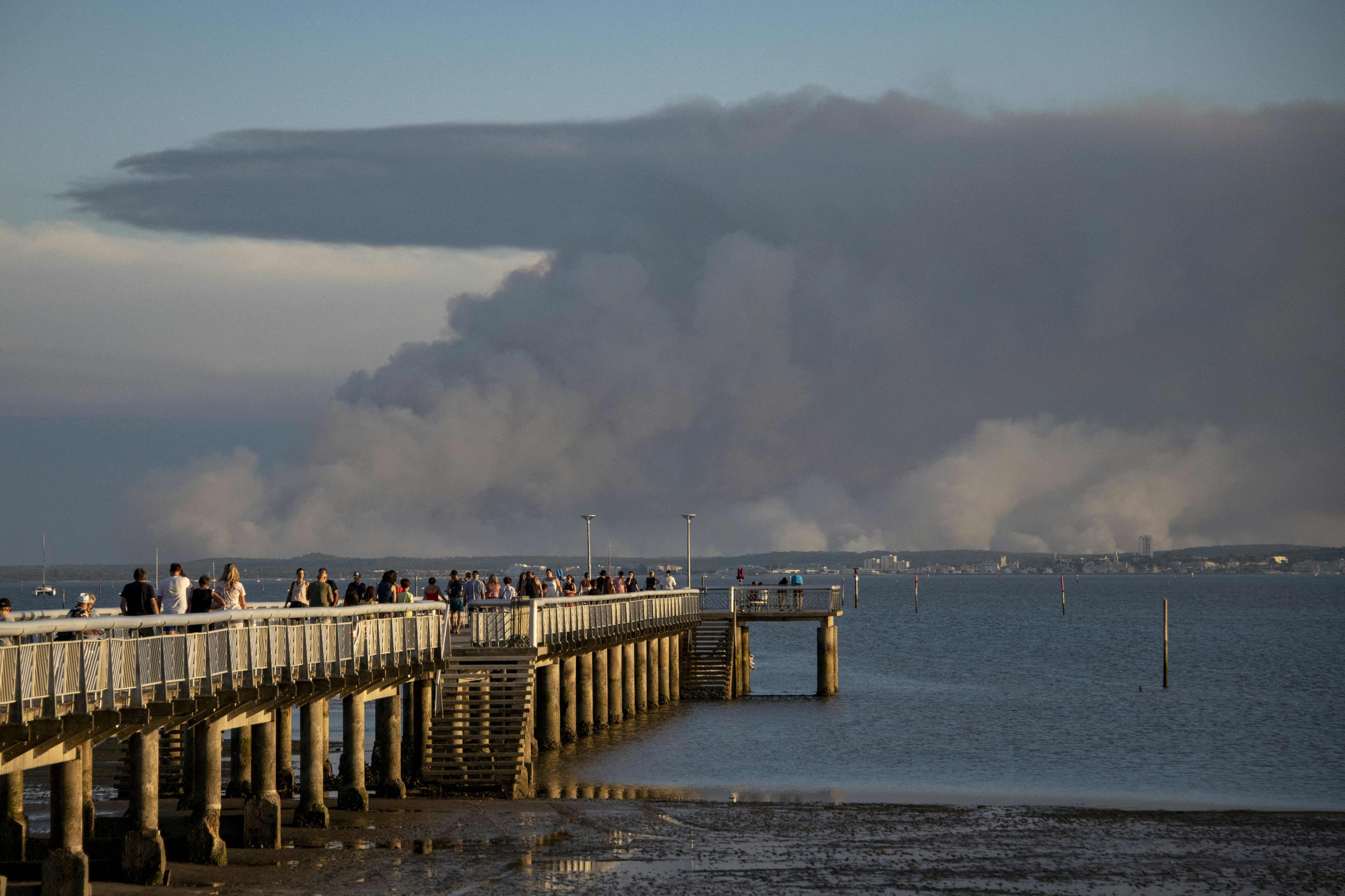 Tourists look at the plume of dark smoke on the shoreline of Arcachon from the peer in Andernos-les-Bains, due to a wildfire in a forest near La Teste, southwestern France, on July 14.