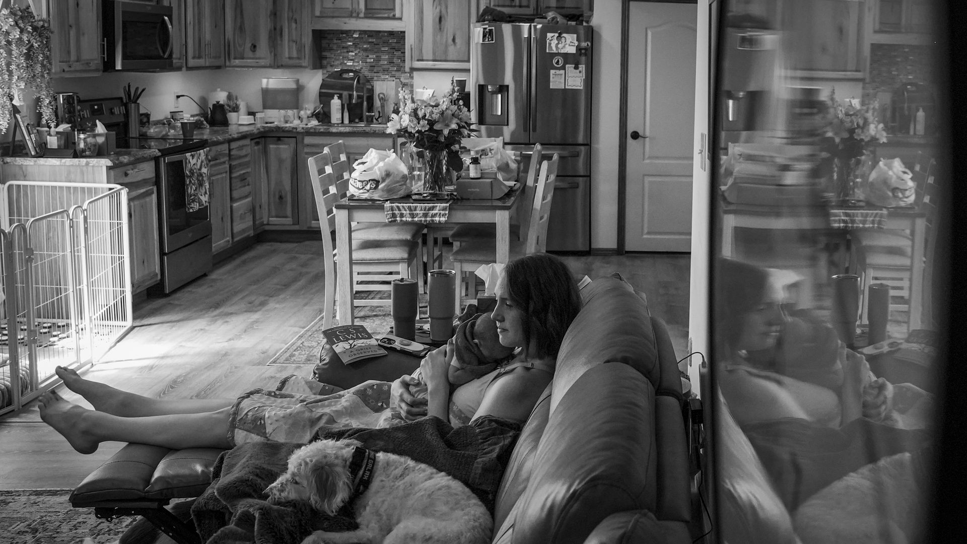 A black and white photo of a woman holding a baby and sitting on a couch.