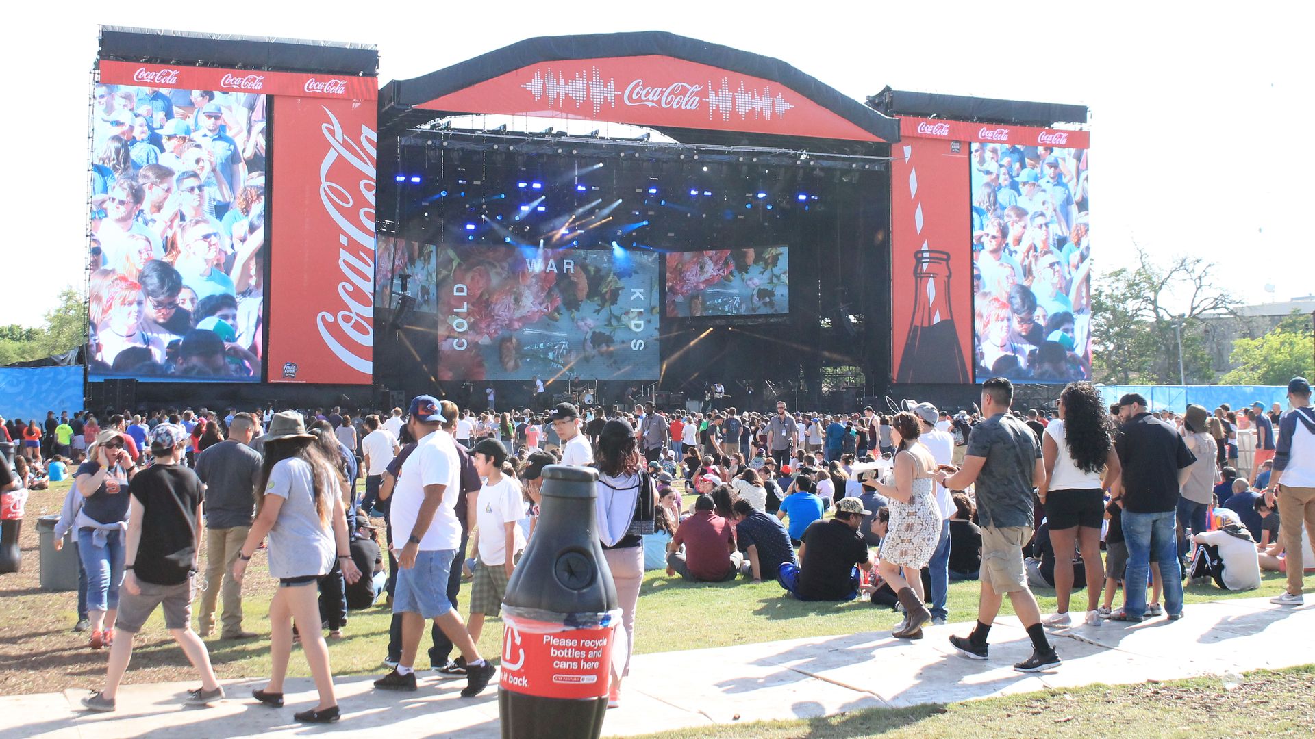 A crowd of people gather around an outdoor stage.